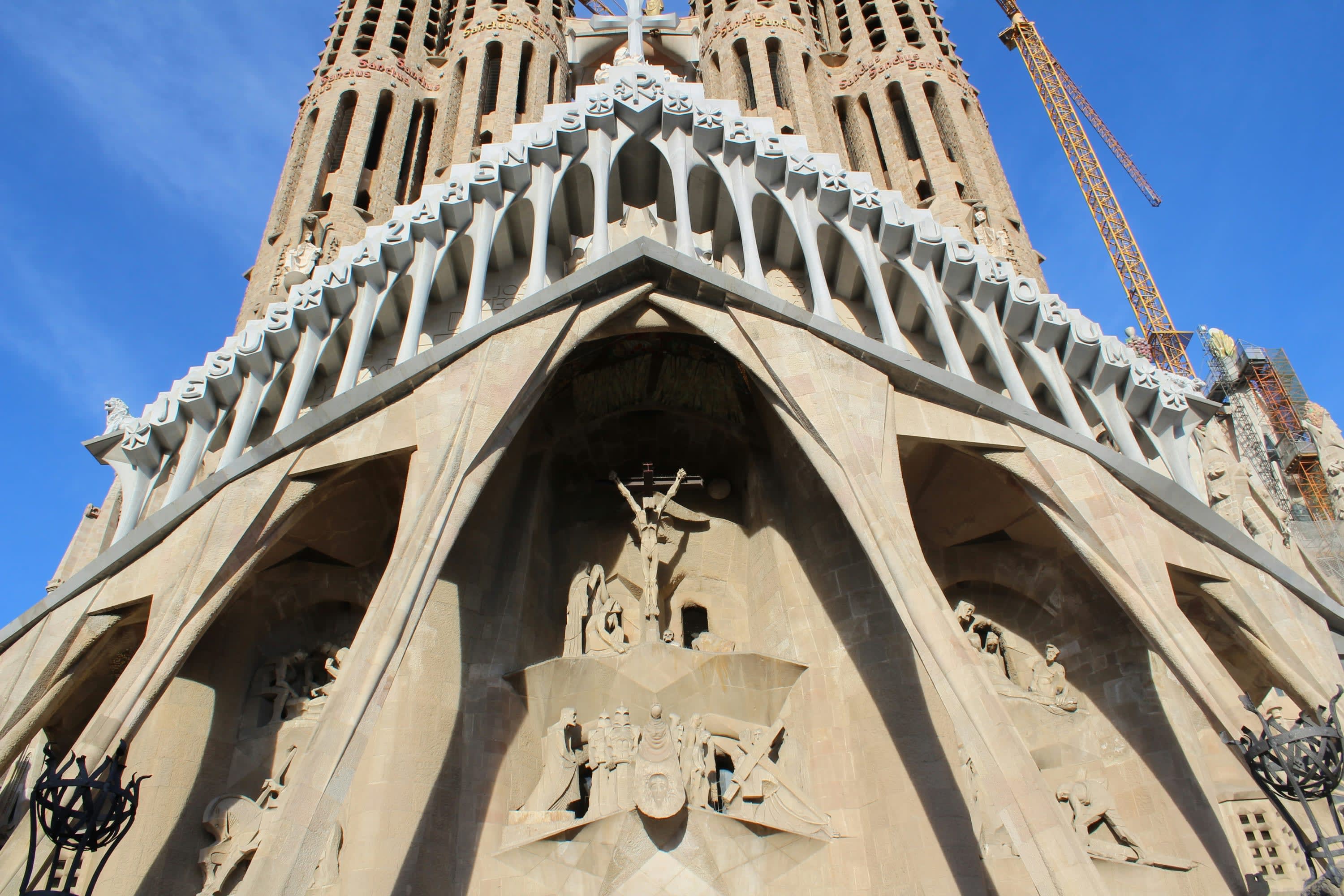 A closeup on the spire of the Sagrada Família. Out of focus, a worker works on the structure highlighting the landmark's continued construction