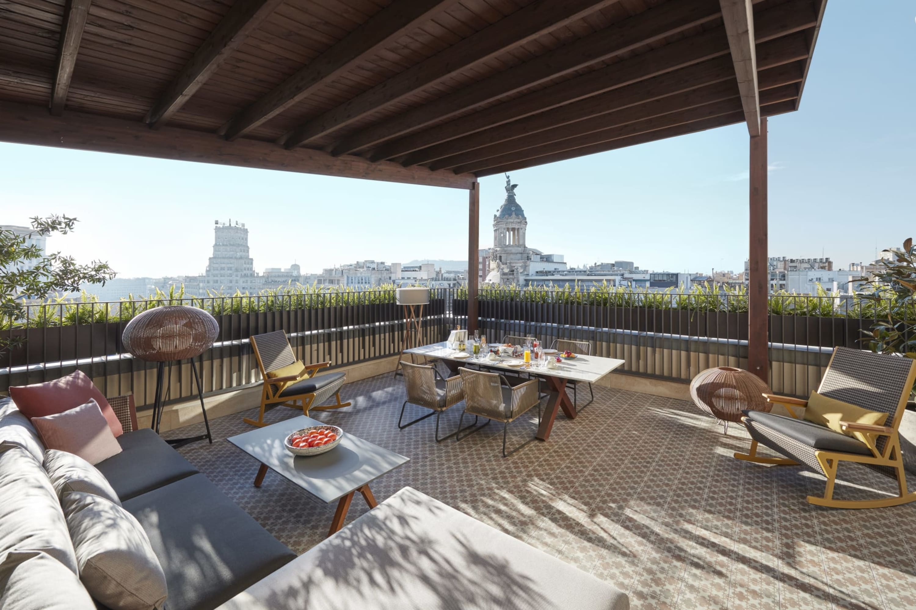 A chic terrace space under a contemporary wooden awning. In the distance, historic landmarks are visible