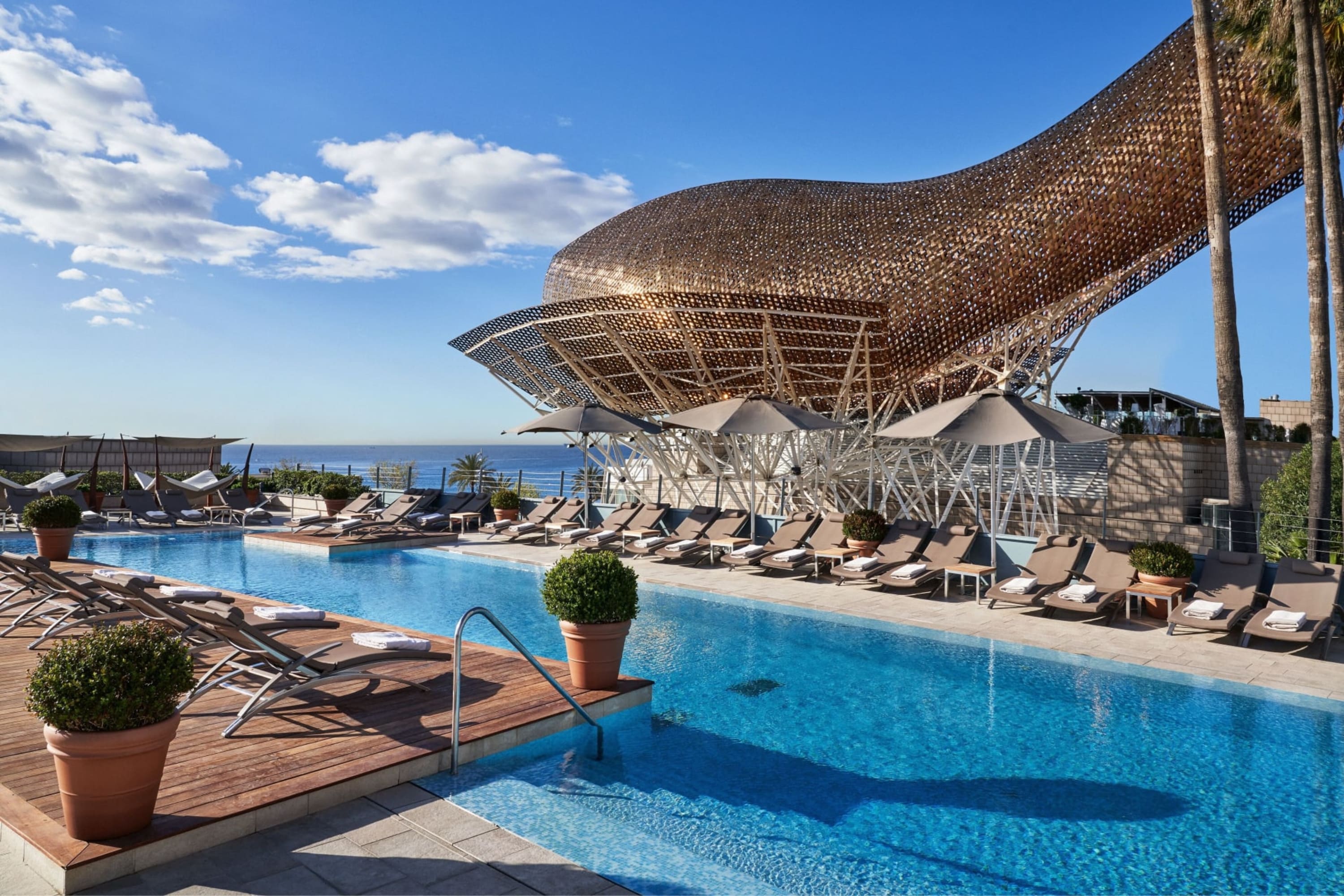 A posh pool area with a large abstract art installation and the Mediterranean in the background