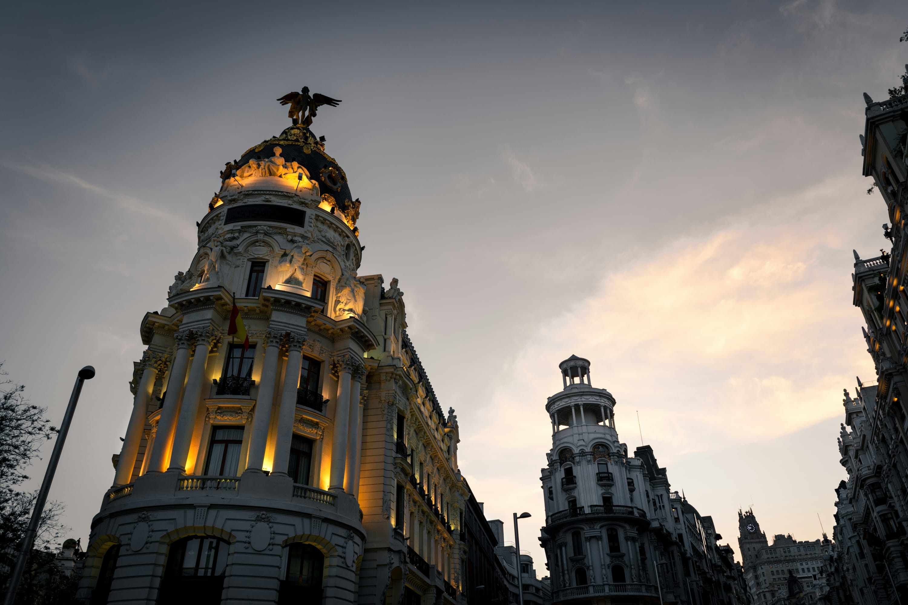 At twilight, lights in a historic building with an angel statue on top contrast with a darkening sky