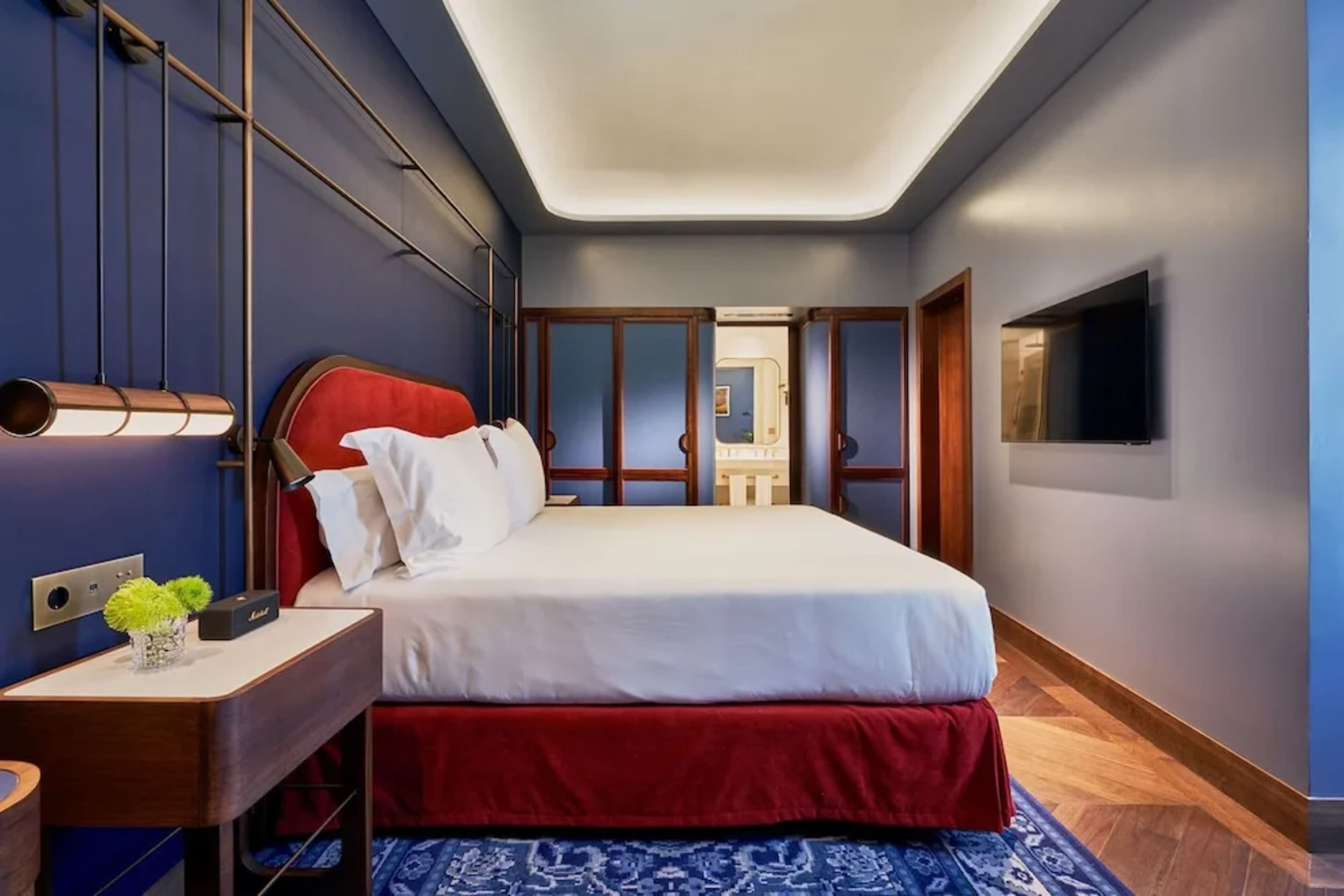 Stylish hotel room with deep-blue wall accent, modern furniture and a large white bed