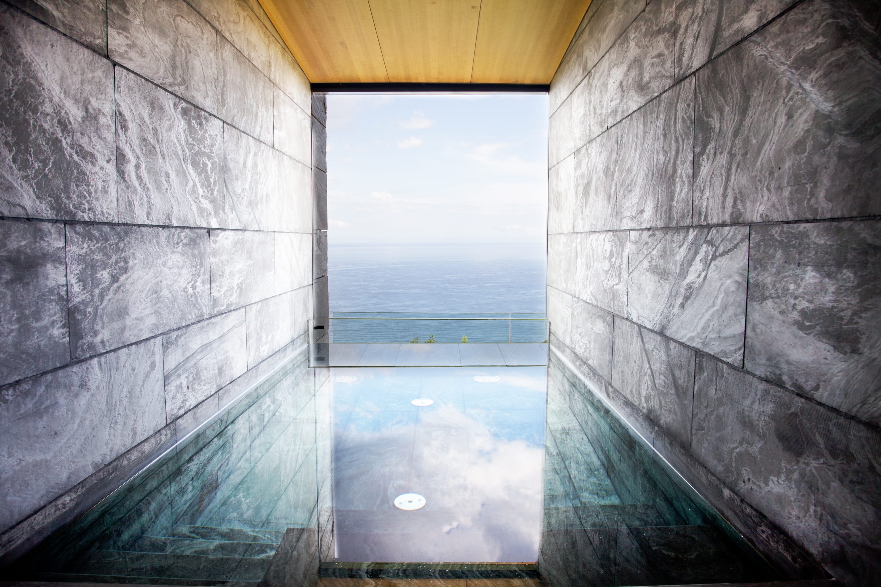 Gradient-textured stone walls provide privacy for a private pool with contemporary sapphire tiles. On the opposing side, the pool leads to a private balcony