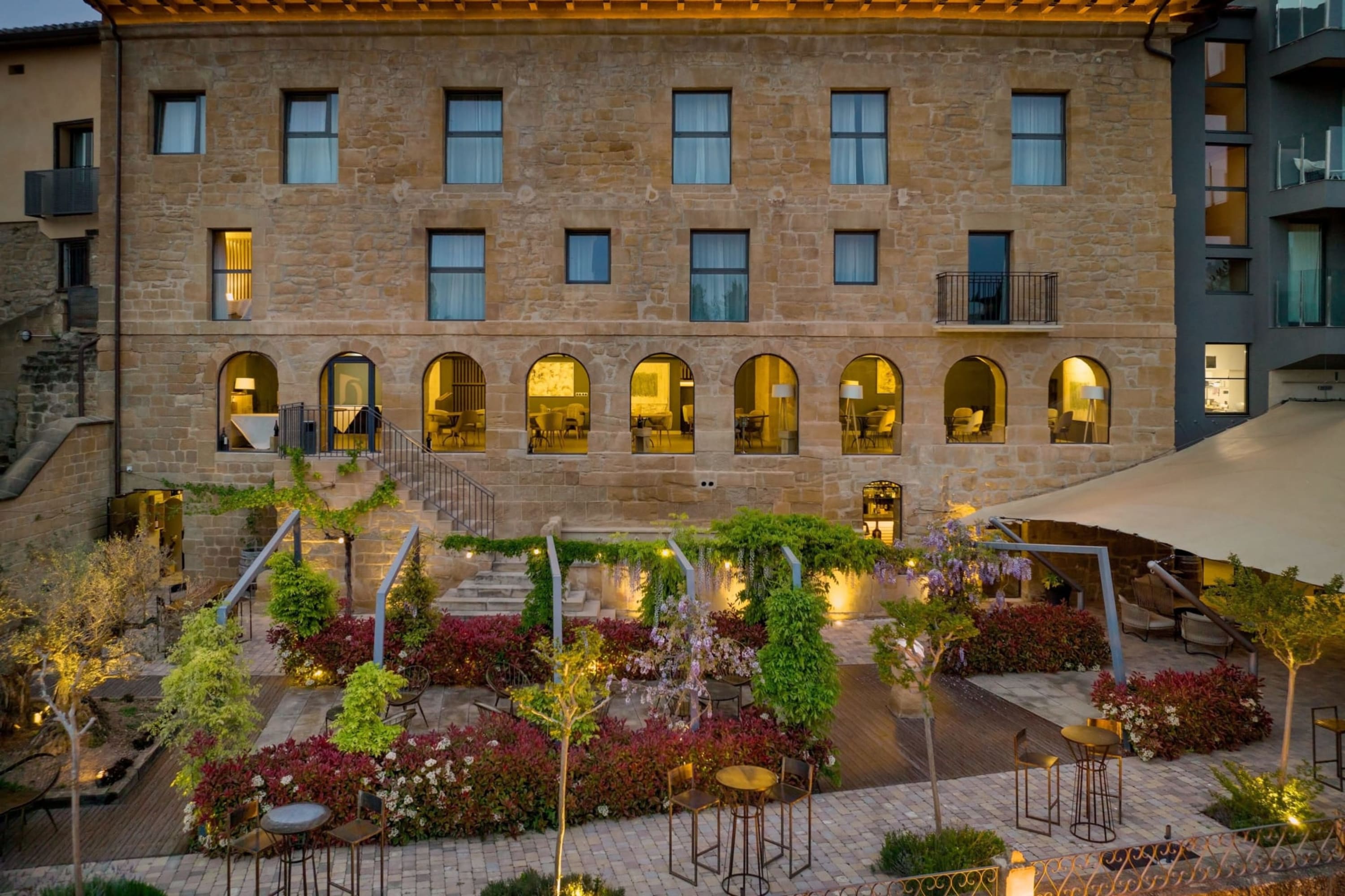 Well-manicured gardens and posh, high bar tables in front of a historic-looking stone structure
