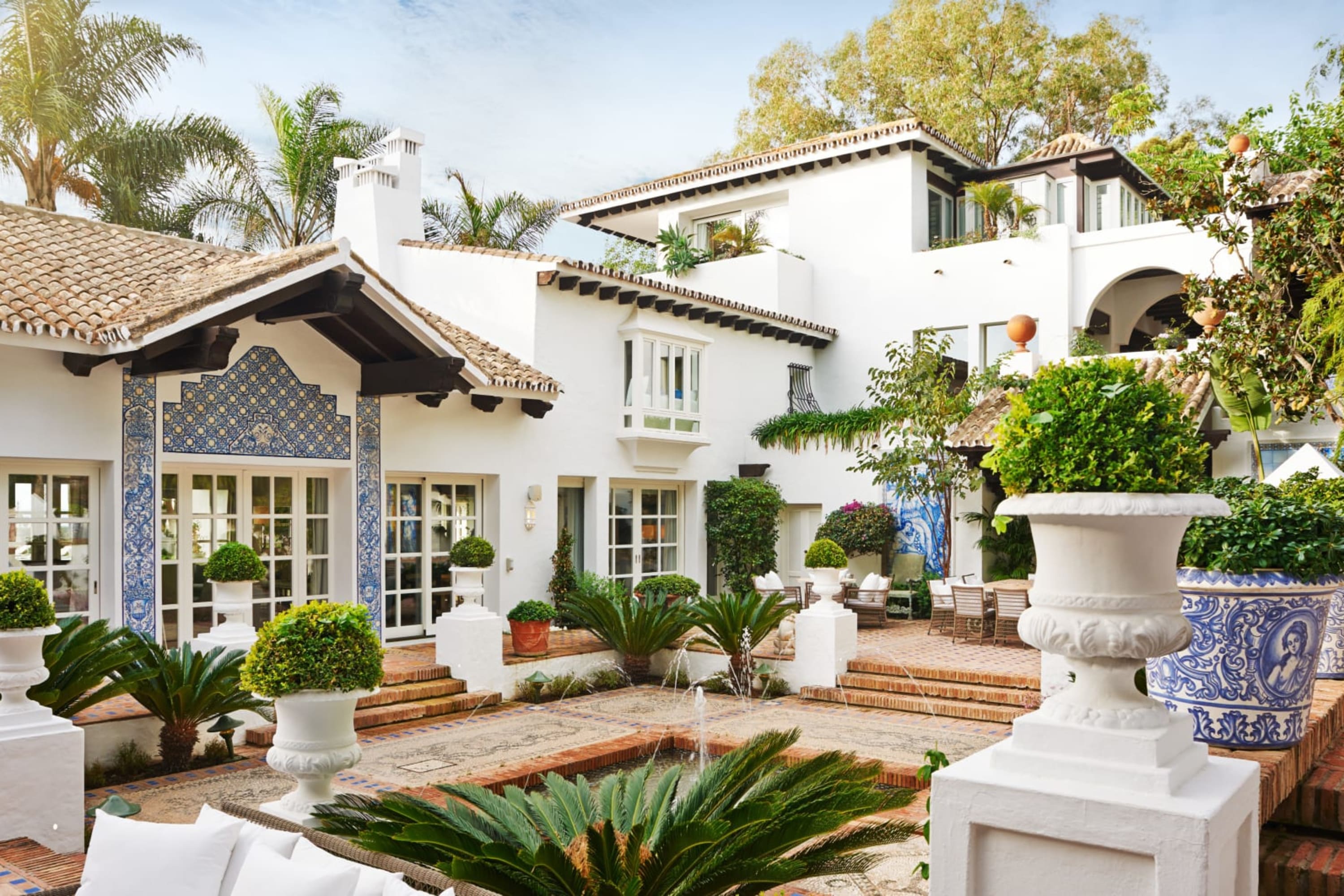 A mansion-sized private villa with whitewashed walls and a water fountain, tons of greenery and art