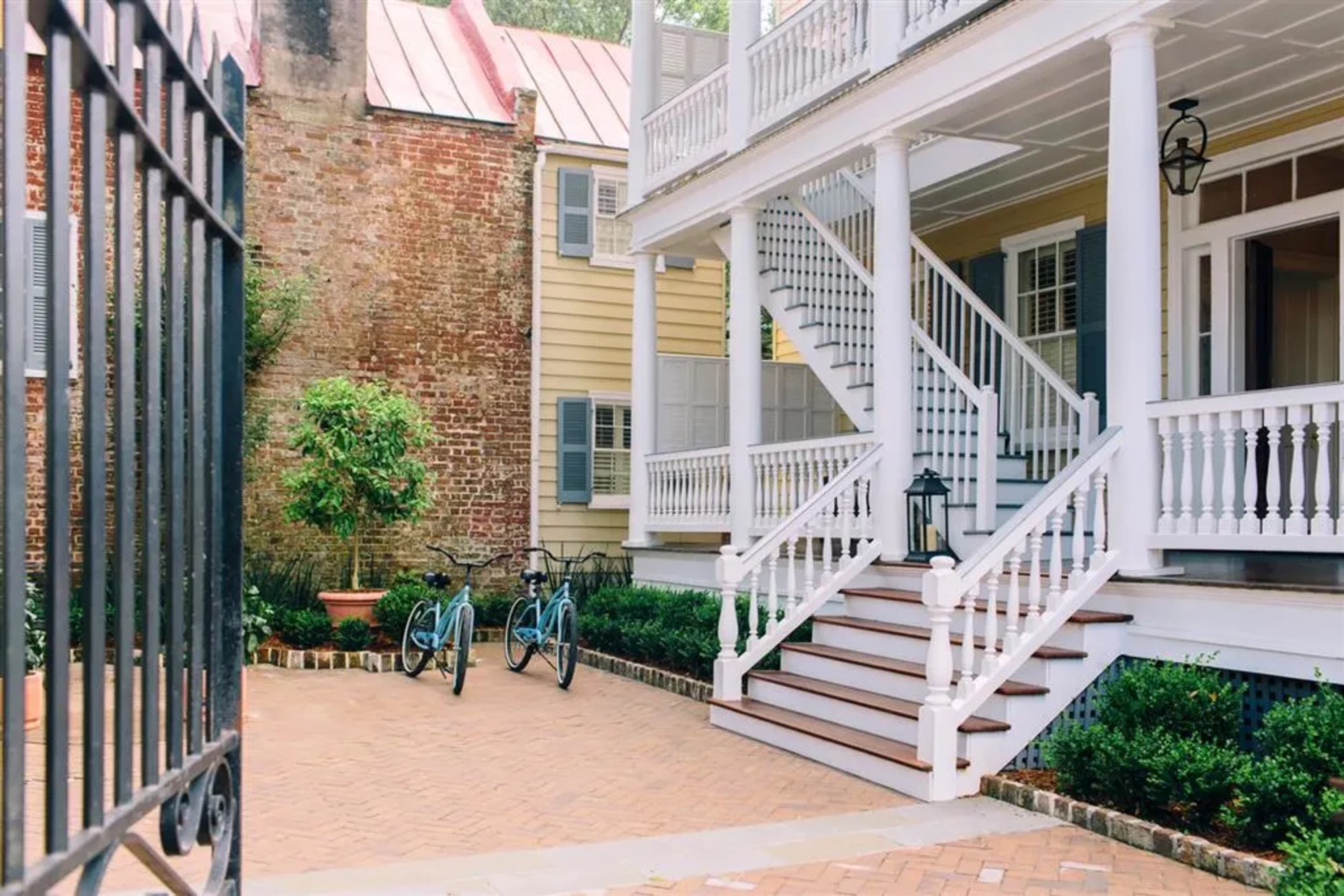 Brick courtyard with open wrought-iron fence. White wooden staircases lead to hotel units