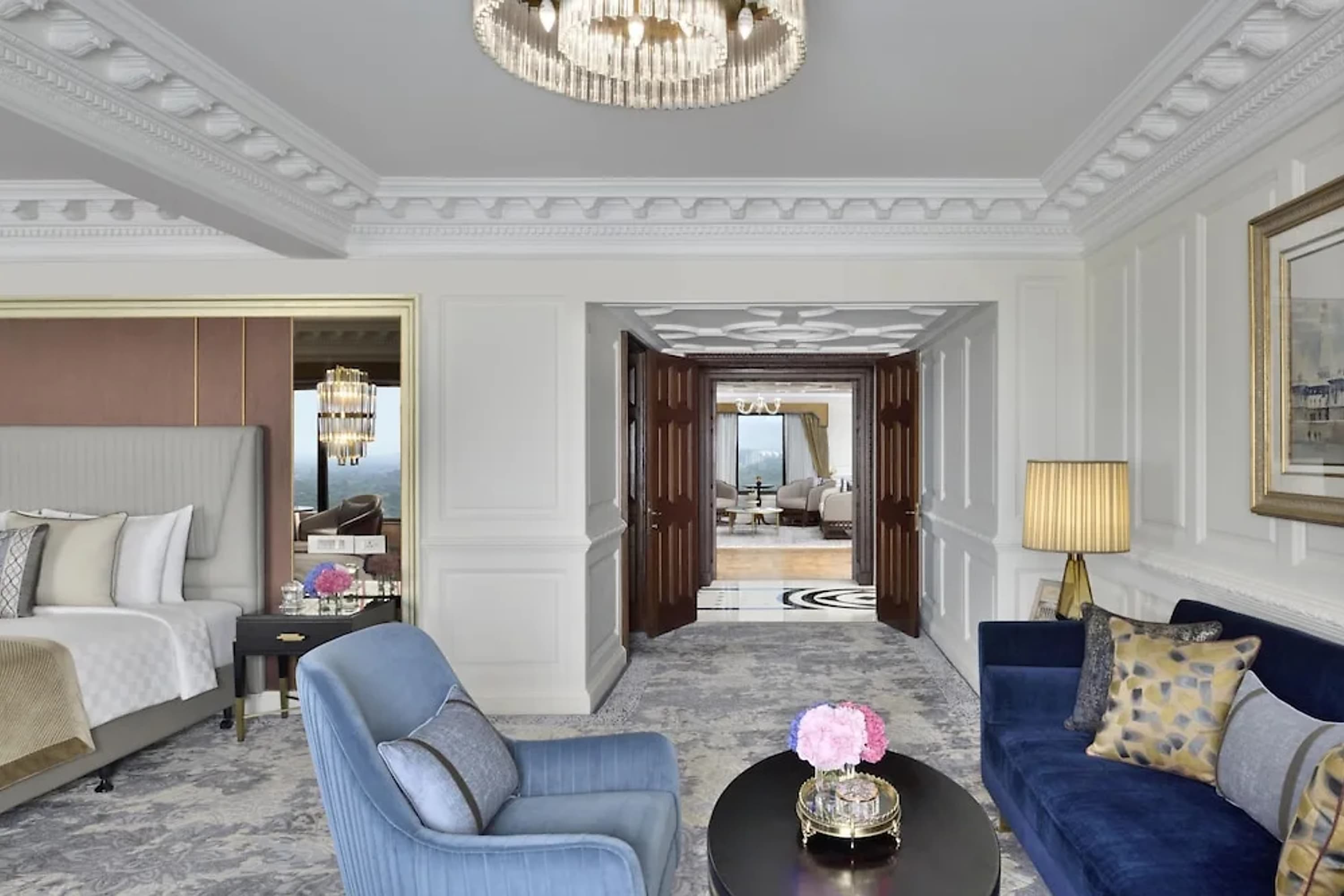 Spacious and luxurious hotel bedroom part of a larger suite. A marble hallway is visible out the door, leading to another living room or bedroom
