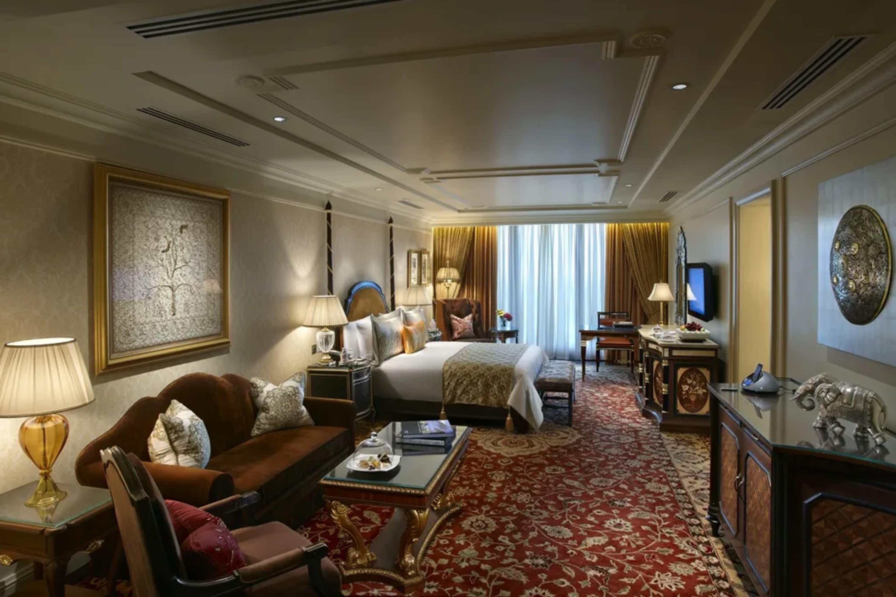 Moody but elegant hotel room with a large Persian rug, opulent fabrics and patterns, and vintage furniture