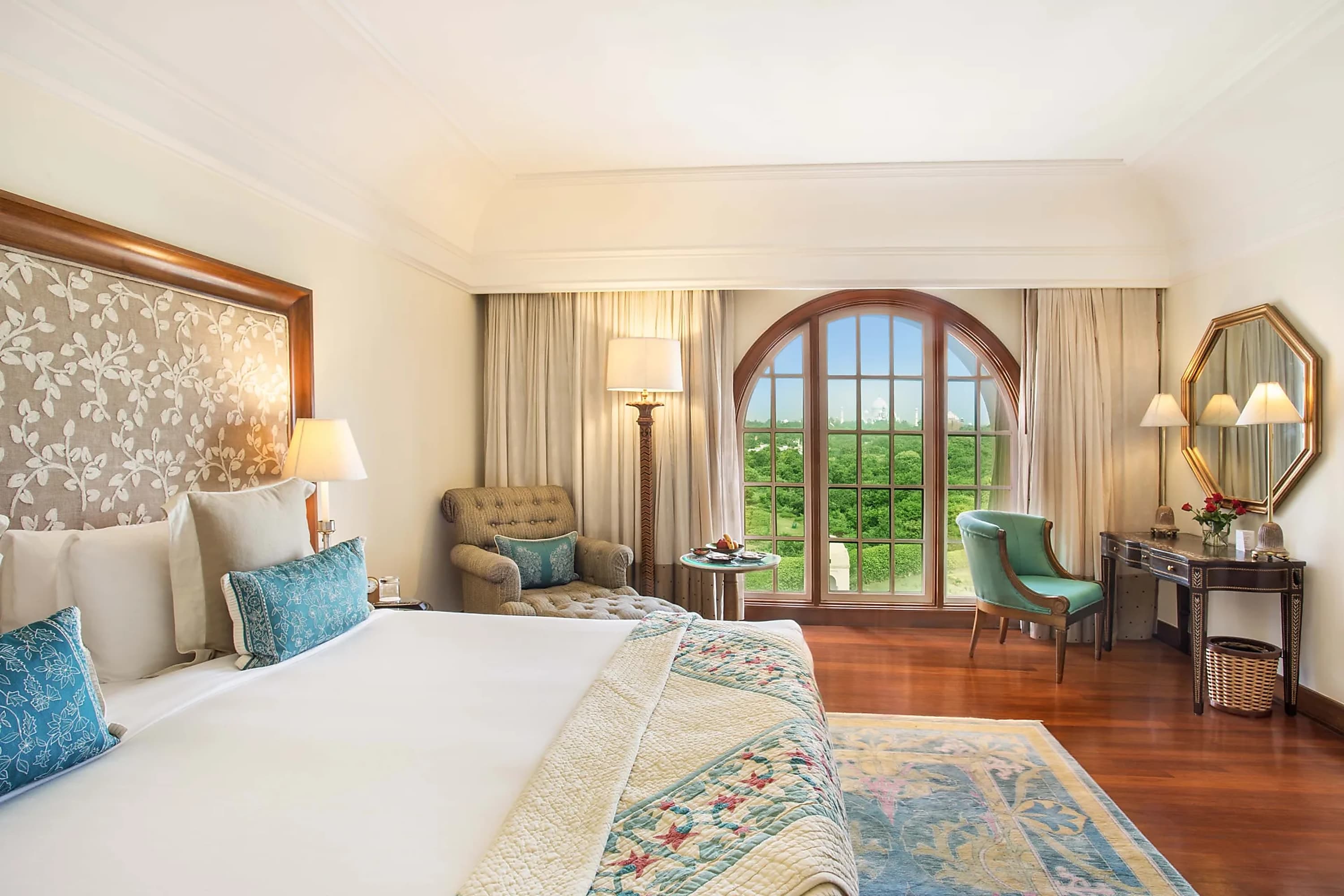 Elegant hotel room with hardwood floors and a view of the Taj Mahal and forest through an arched window