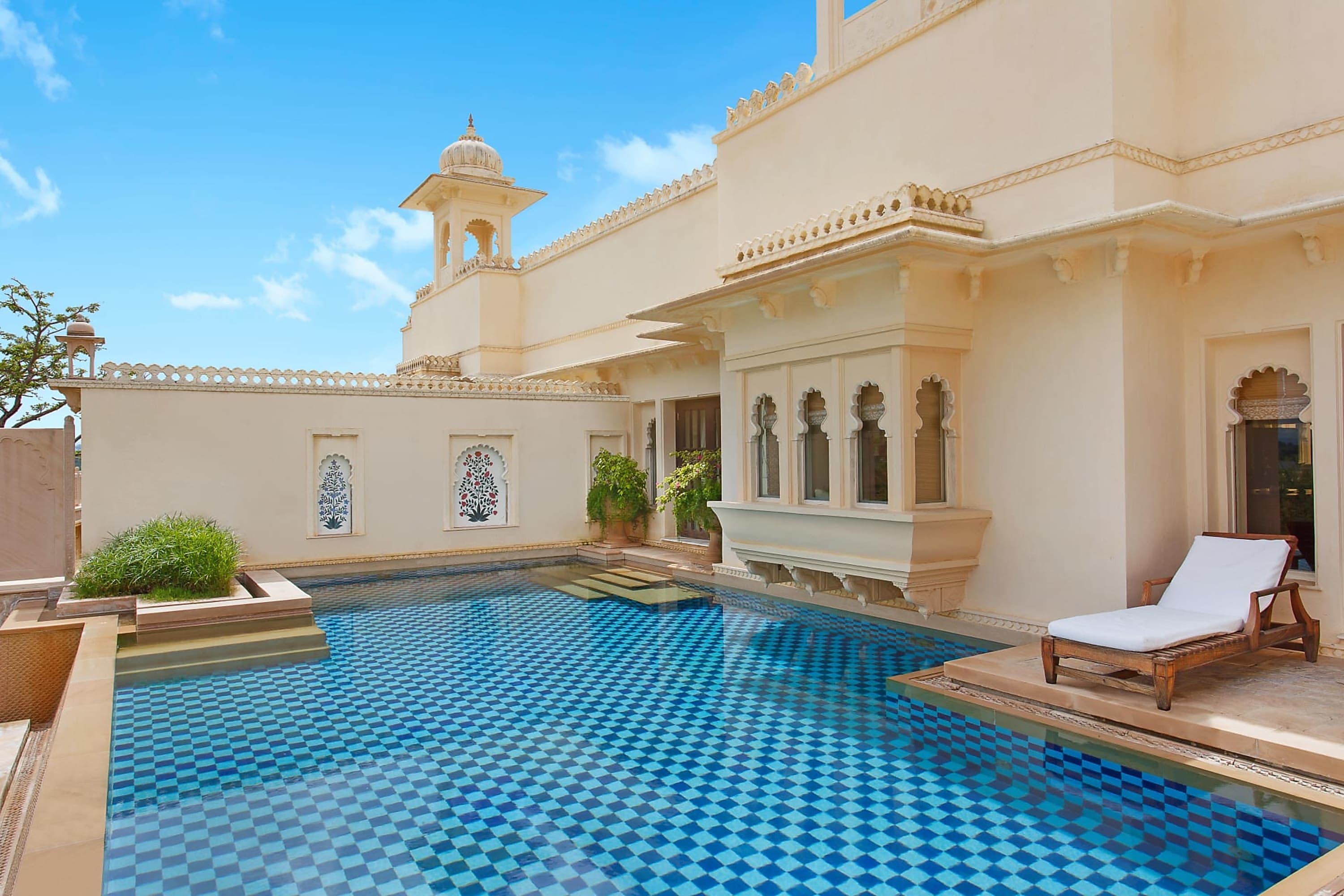 Large private pool with intricate tiles on the bottom extending from a palace-like building