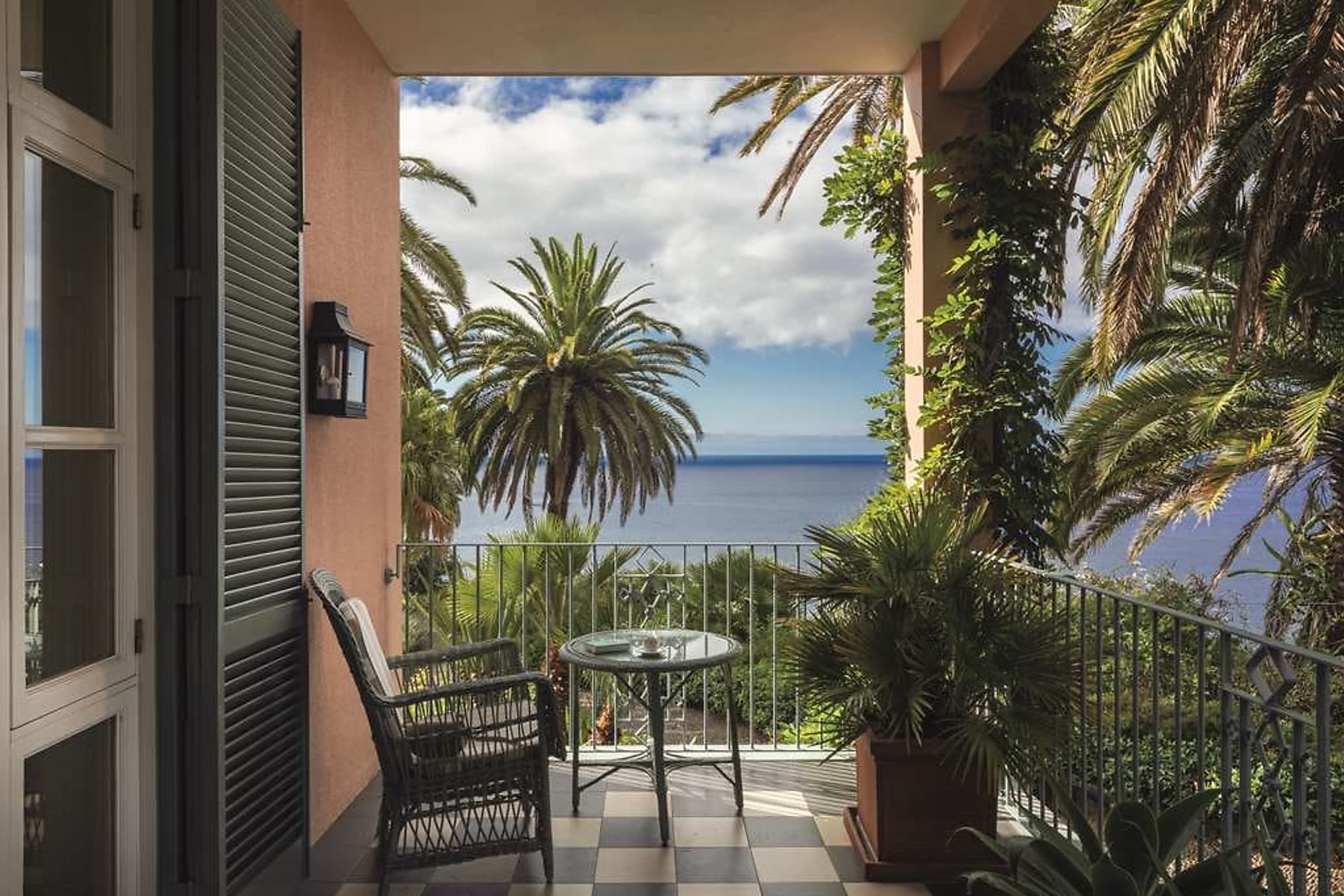 A private balcony with checkboard tiles, lounge furniture, plenty of greenery, iron railing and accents, and a stellar view of the Atlantic
