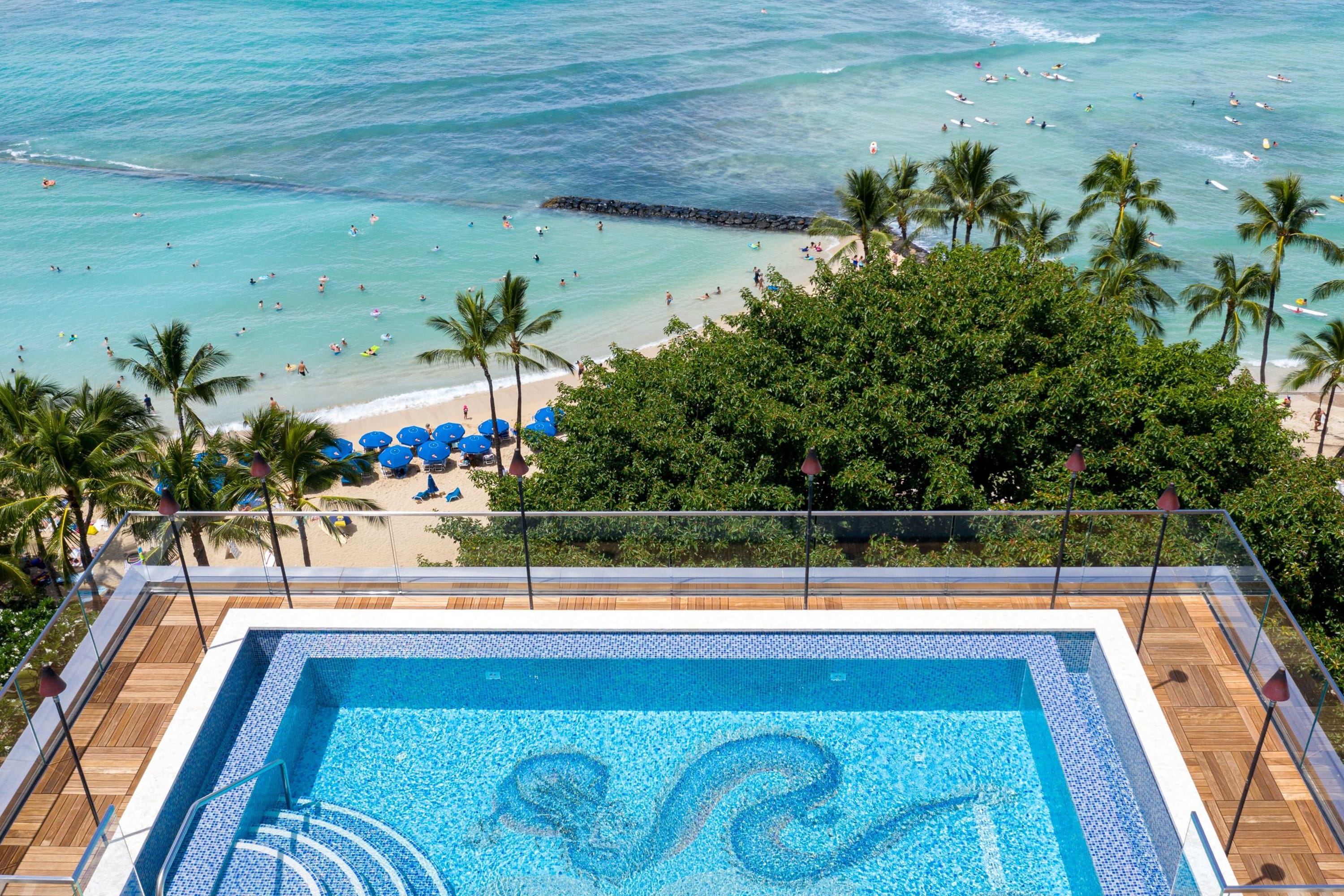 Rooftop pool with tiles shaped like a dragon overlooking Waikiki Beach and dozens of people in the surf