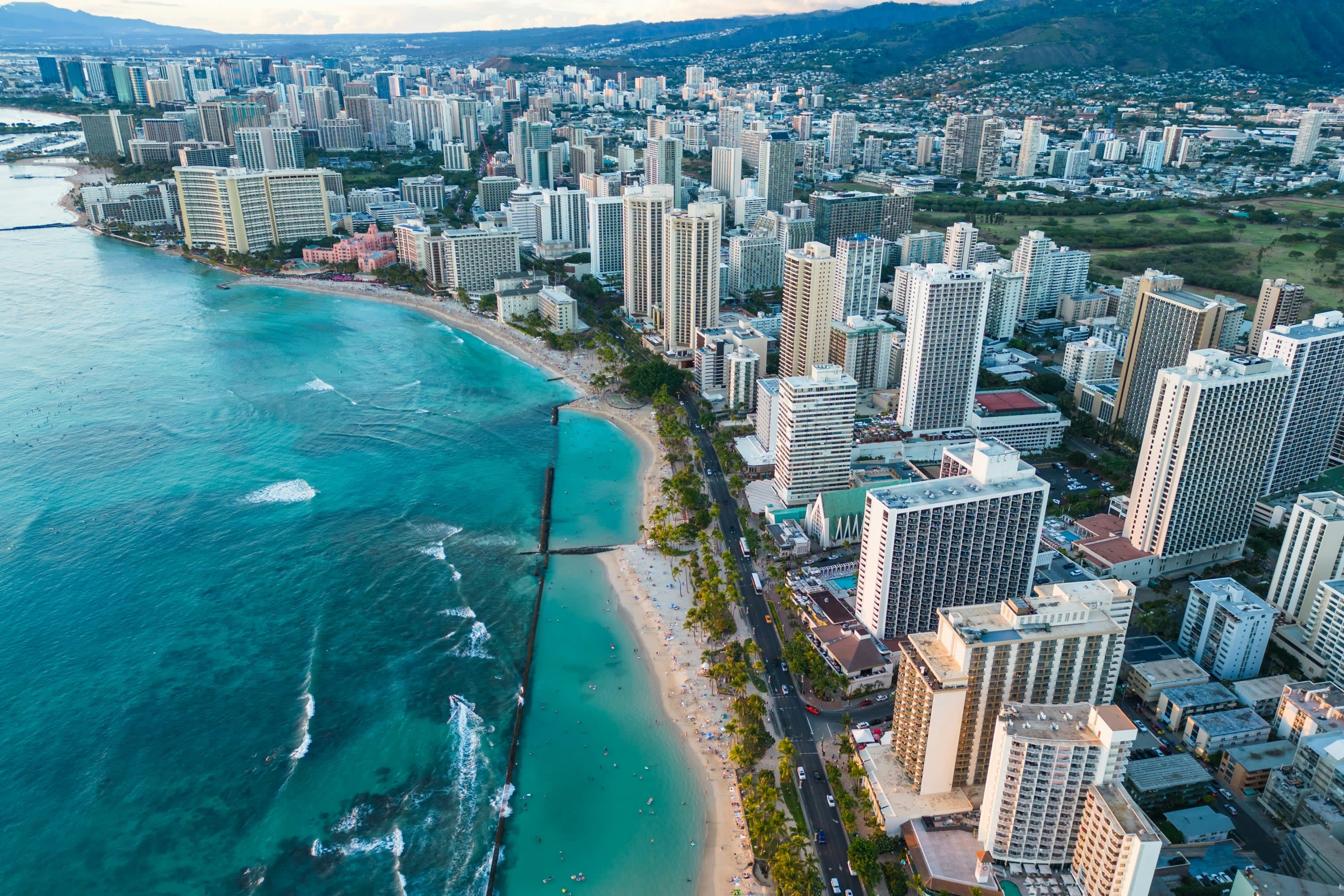 Rows of white high-rises along a beach otherwise surrounded by palm trees on one side and the turquoise waters of the Pacific on the other