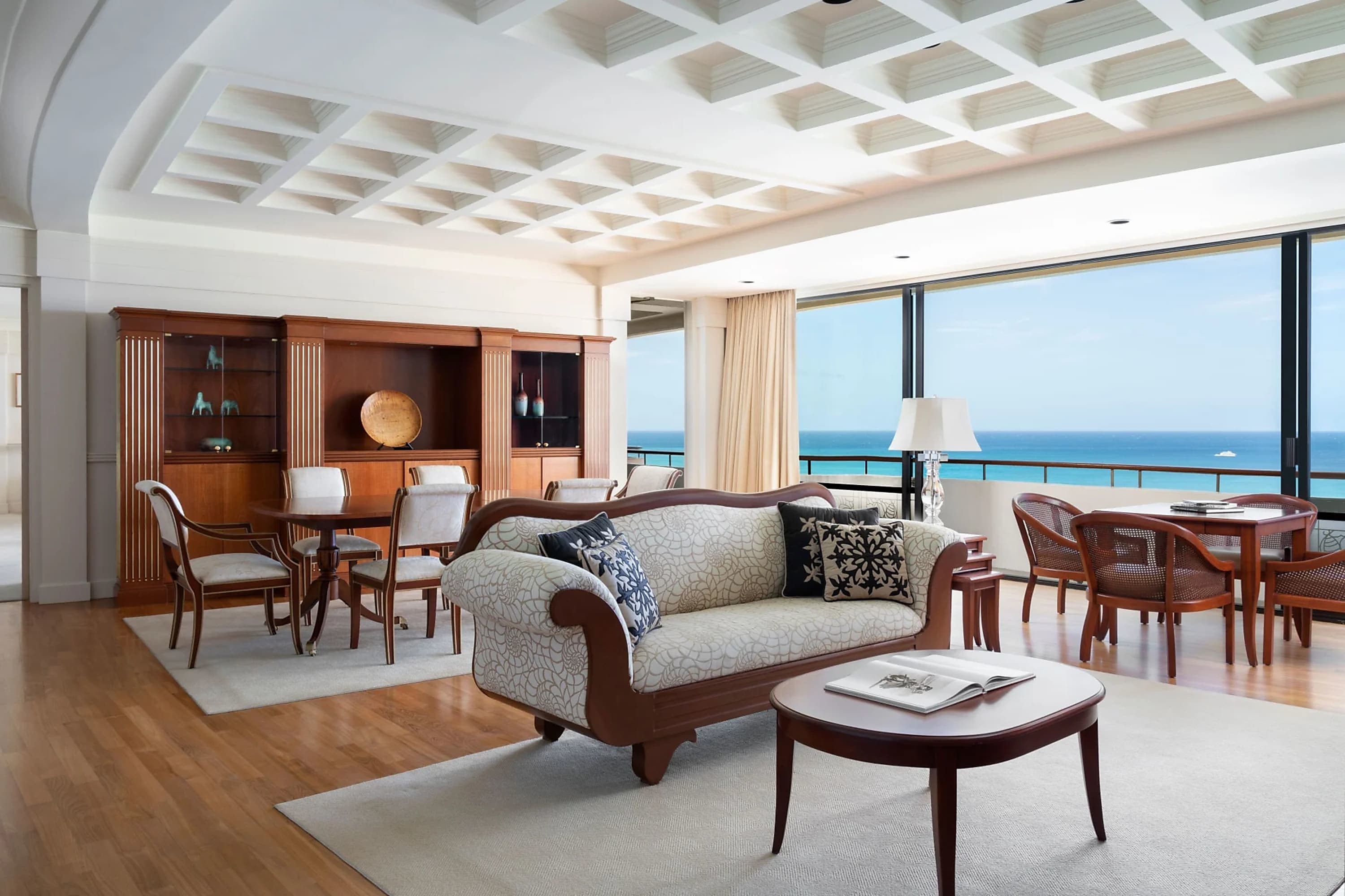 Hardwood floors, chic rugs, vintage custom furniture, intricate geometric ceiling pattern, floor-to-ceiling windows, and eclectic decor in a massive suite with a high-rise view of the ocean