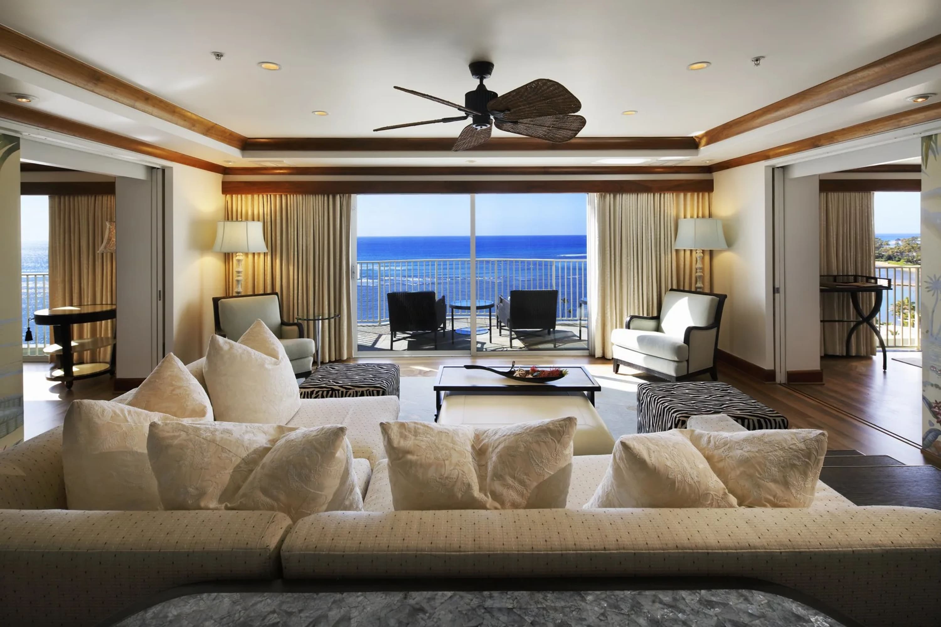 Luxurious suite living room with large sliding glass doors (draped on far sides) opening up to a private ocean-facing balcony