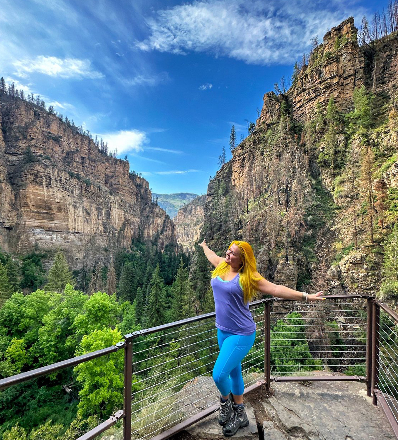 Natalia posing at a lookout point on a hike with a beautiful sunny valley filled with trees in the background