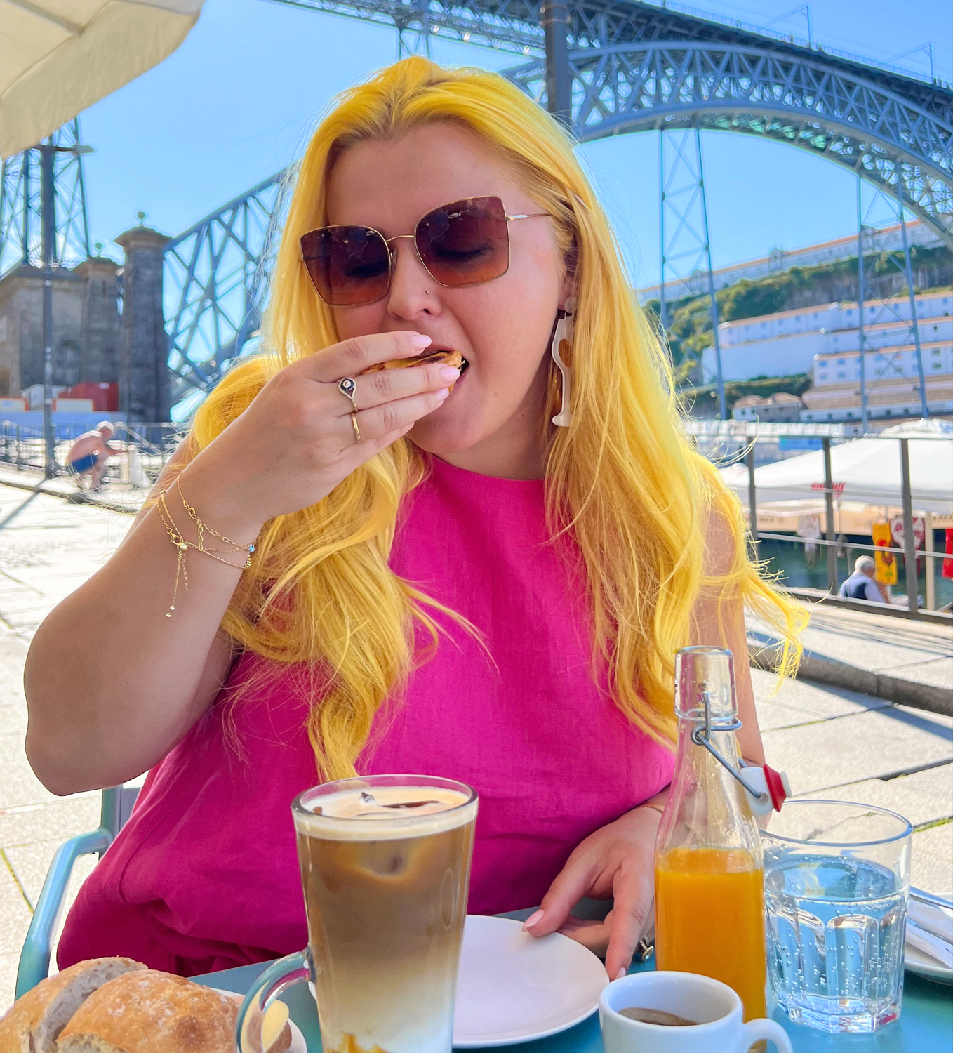 Natalia wearing sunglasses and pink top while eating breakfast and enjoying coffee outdoors