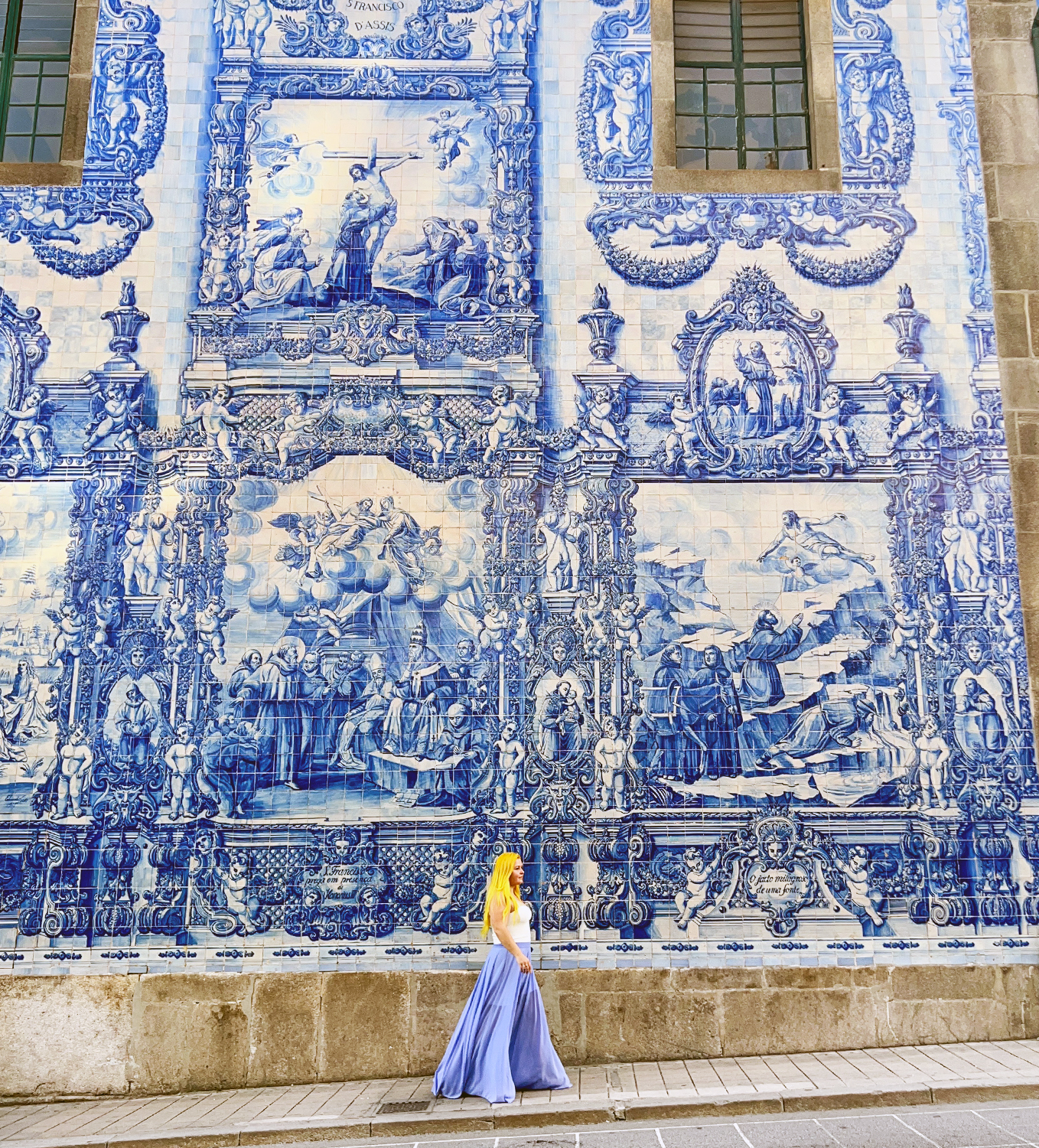 Natalia wearing a blue skirt and walking on the sidewalk in front of a large blue and white mural
