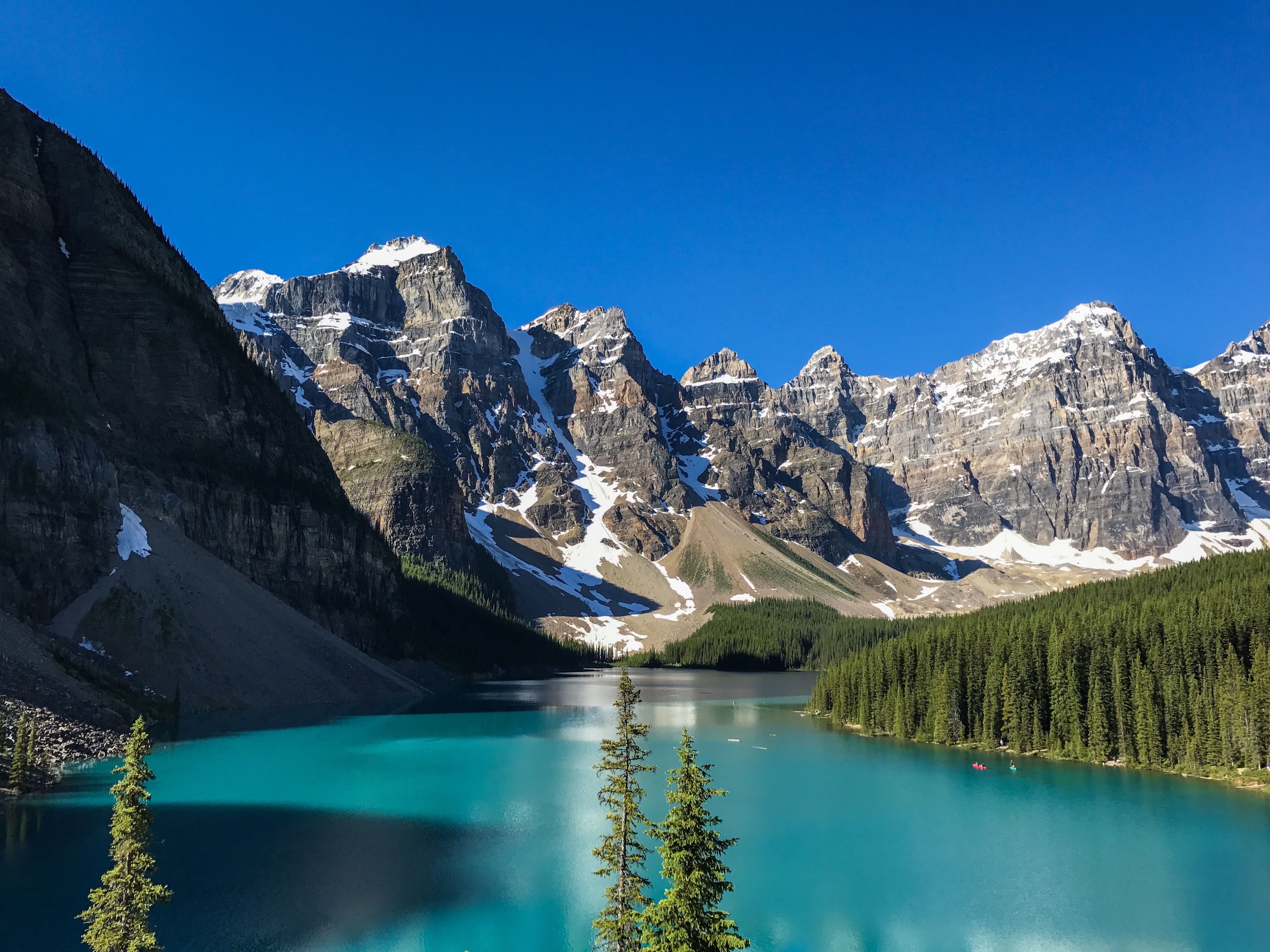 A beautiful view of a turquoise body of water with snow-capped mountains and greenery around