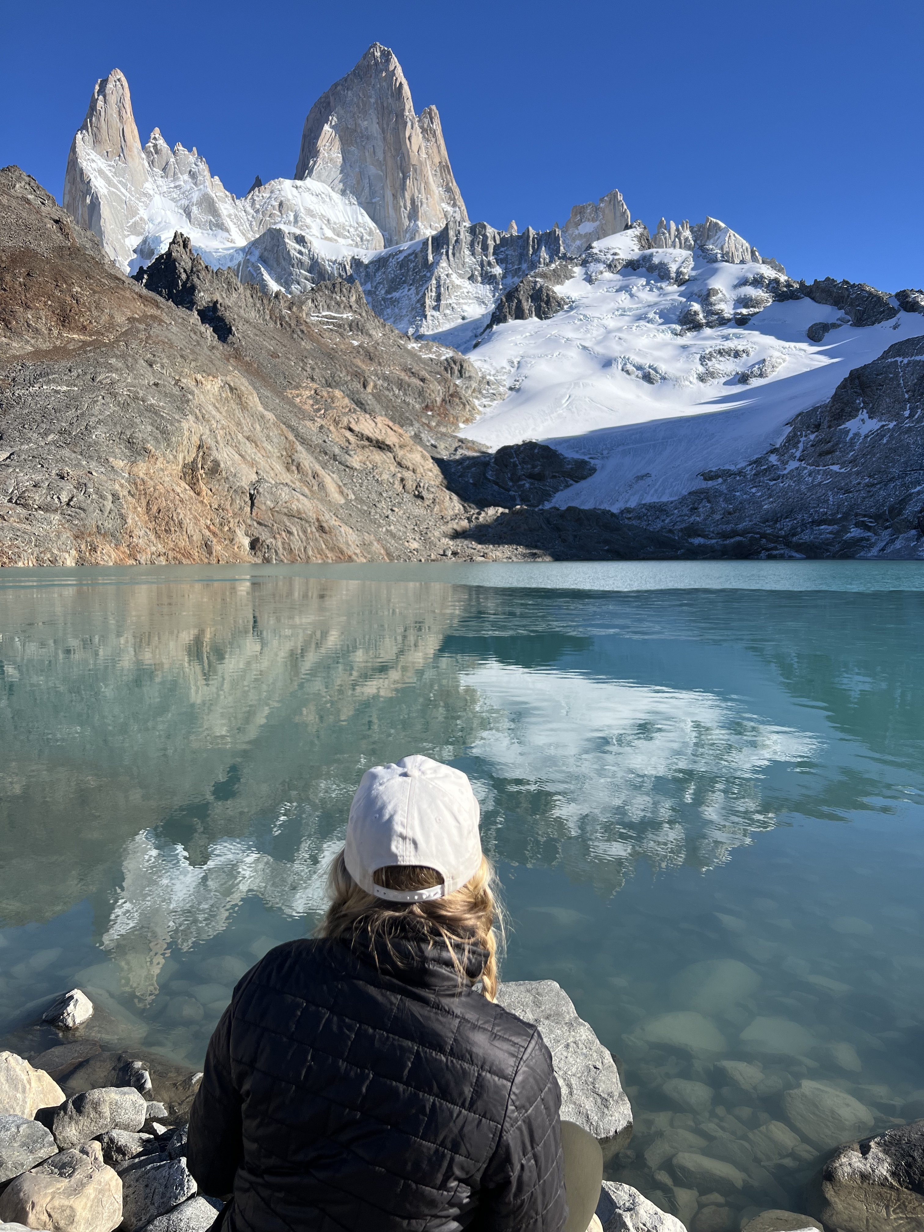 Makenna sitting at the edge of a lake with mountains in the background.