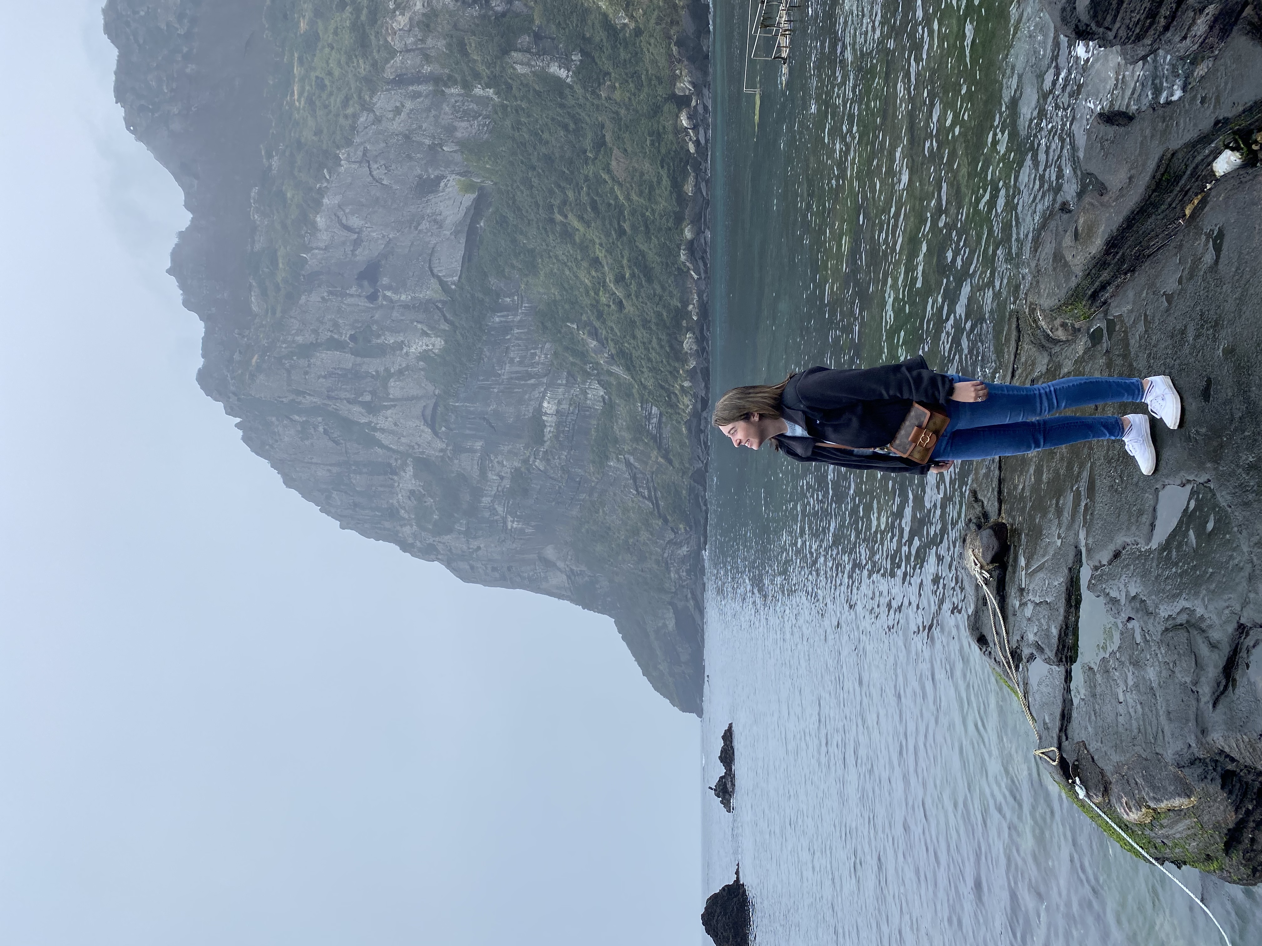 Advisor posing for an image on a rock formation with the ocean in the distance on a cloudy day.