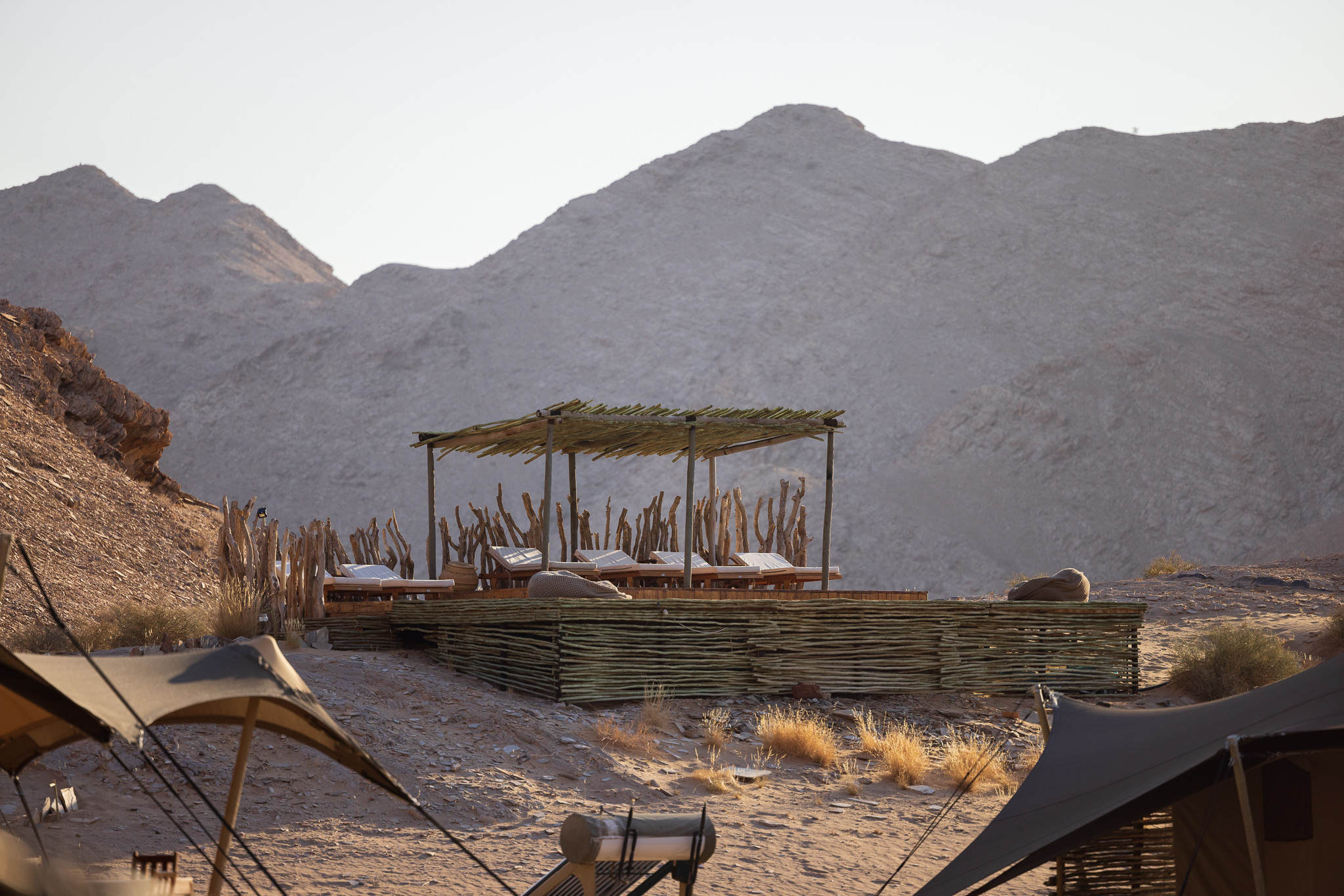View of a wooden platform with lounge chairs and a thatched roof with a beautiful Mountain View in the background