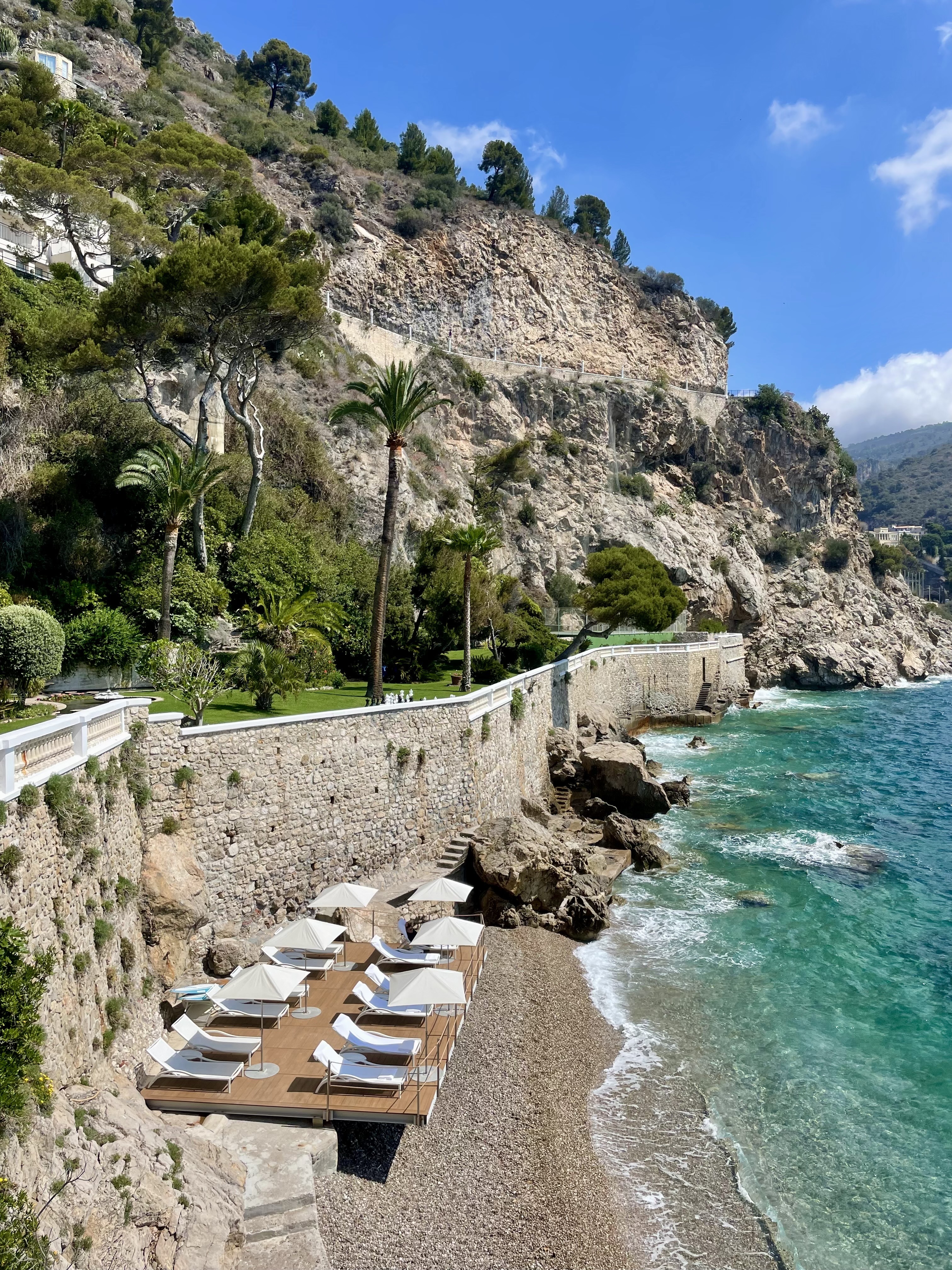 Beautiful view of blue sea and dramatic coastline with cliffs and lounge chairs visible on a rocky beach