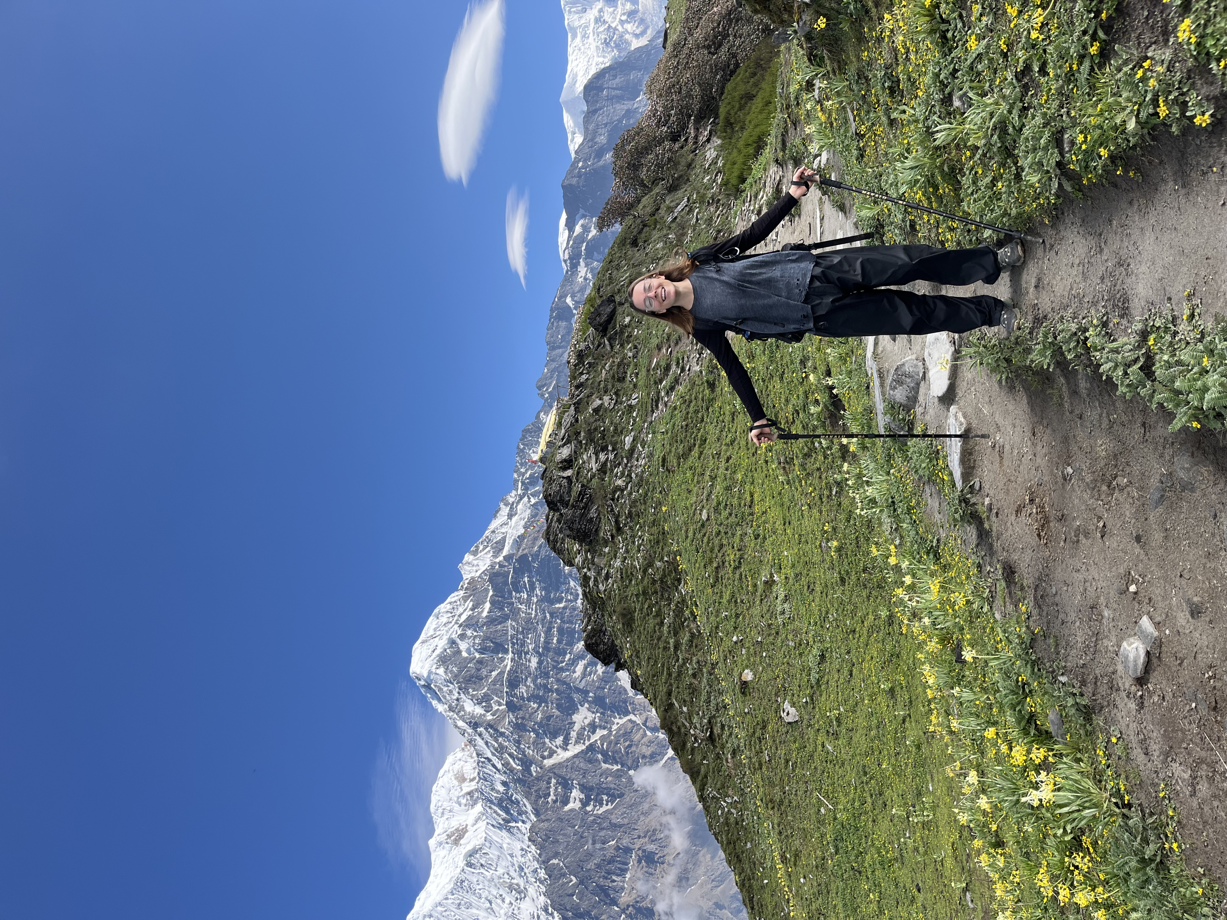 Advisor posing for an image while hiking a mountain range on a sunny day with snow covered mountains in the distance.