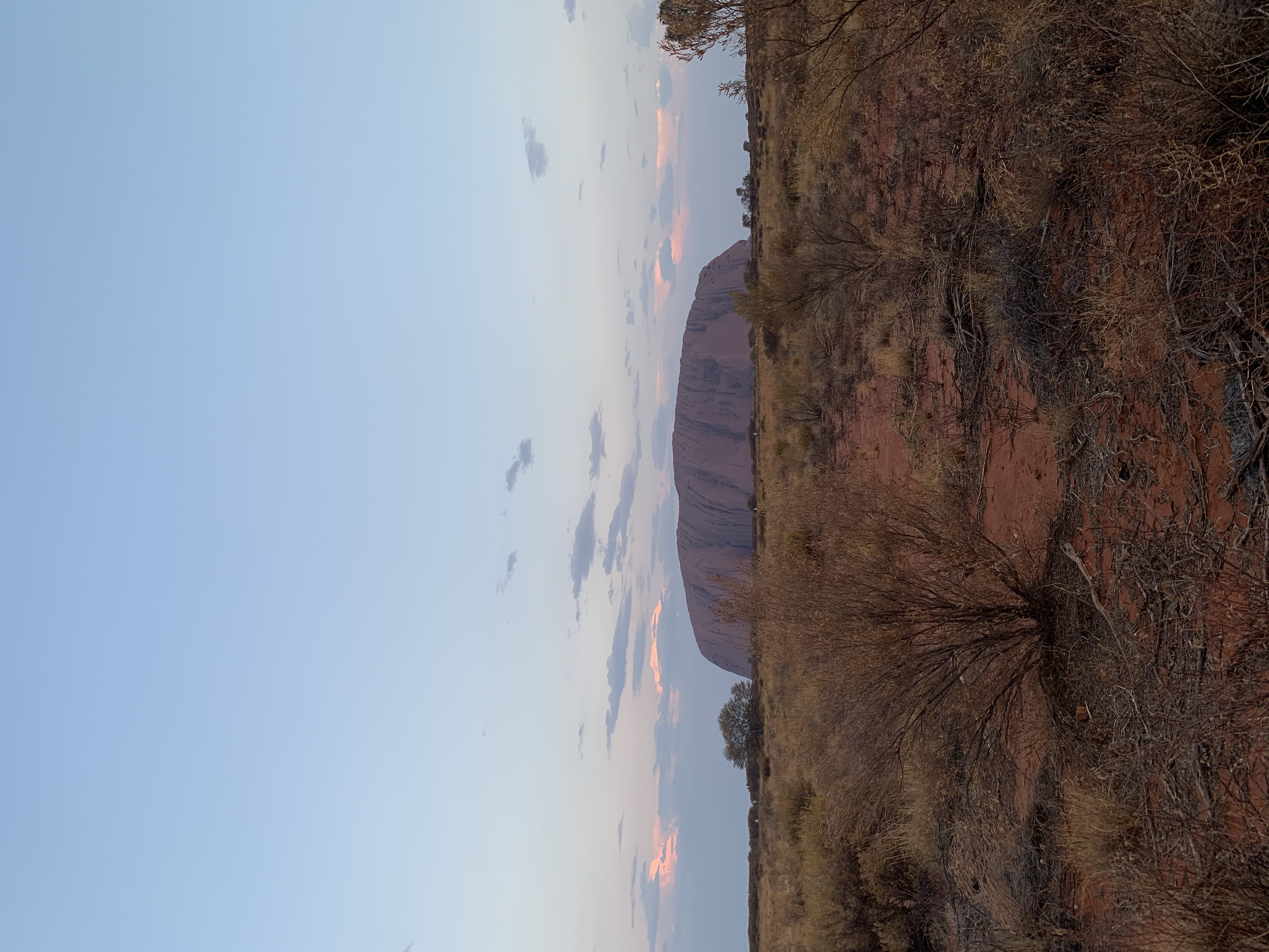 A view of a desert setting at dusk with a rock formation in the distance.