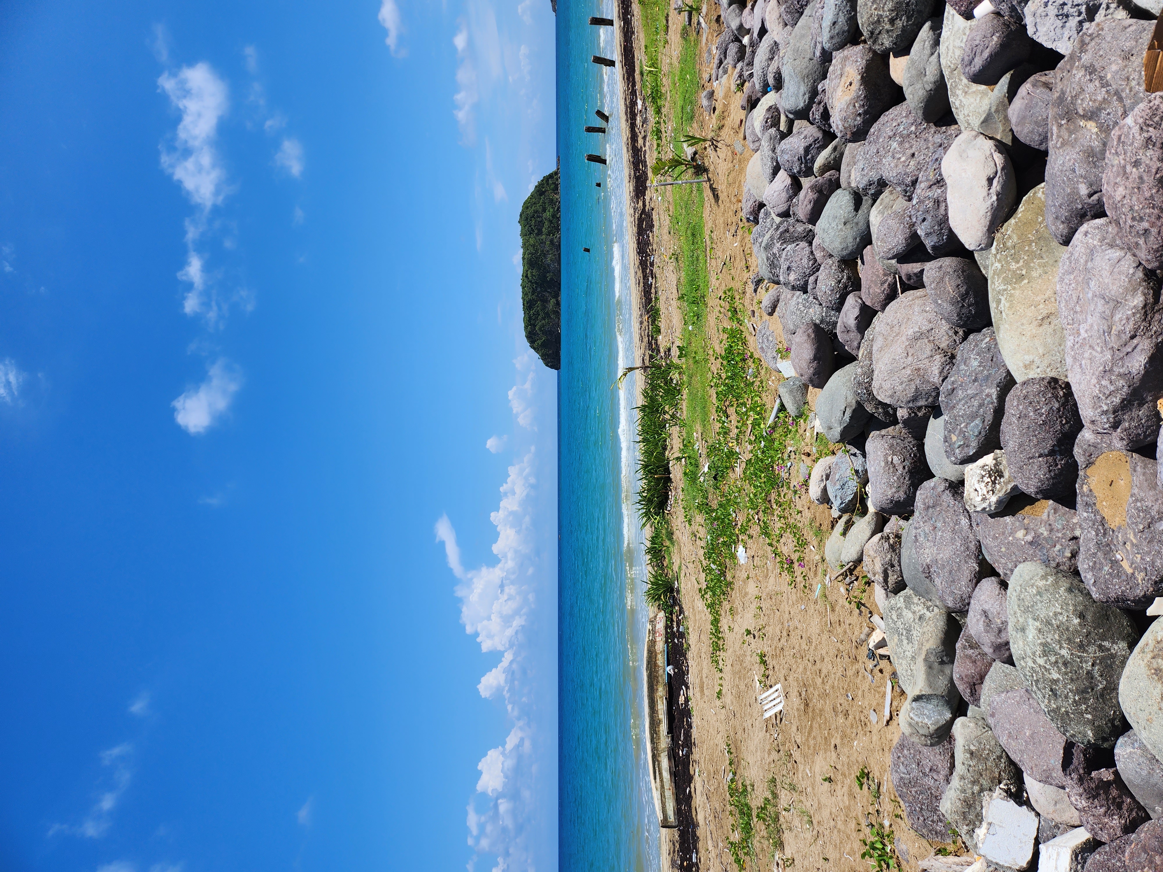 A view of the ocean with a sandy shore and rock formations in the distance on a sunny day.