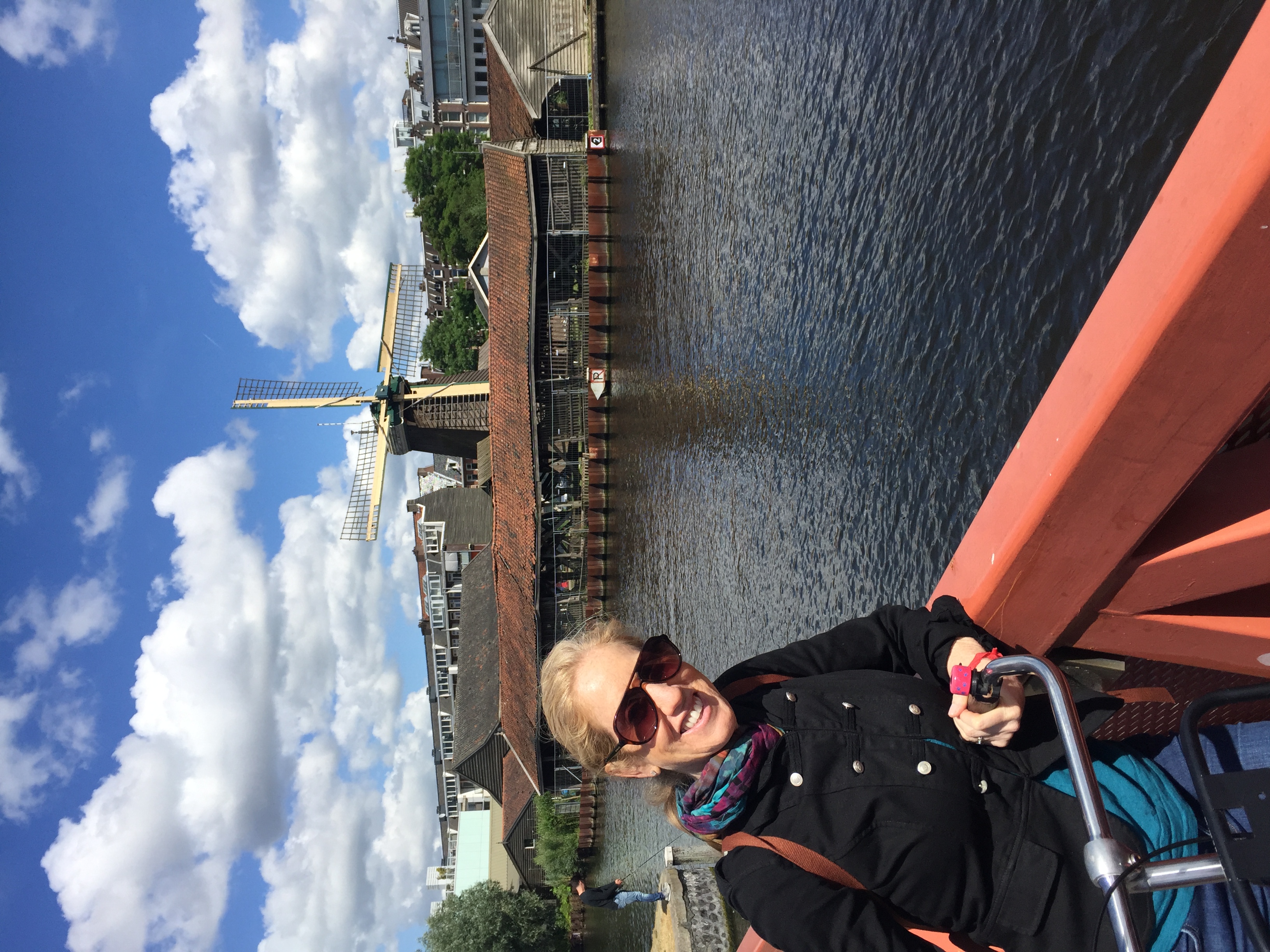 Jill on a bike on a bridge over a canal in Amsterdam, a windmill visible behind her