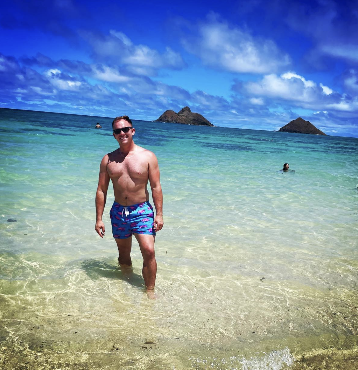 Andrew in swim trunks standing in shallow, clear ocean water on a sunny day