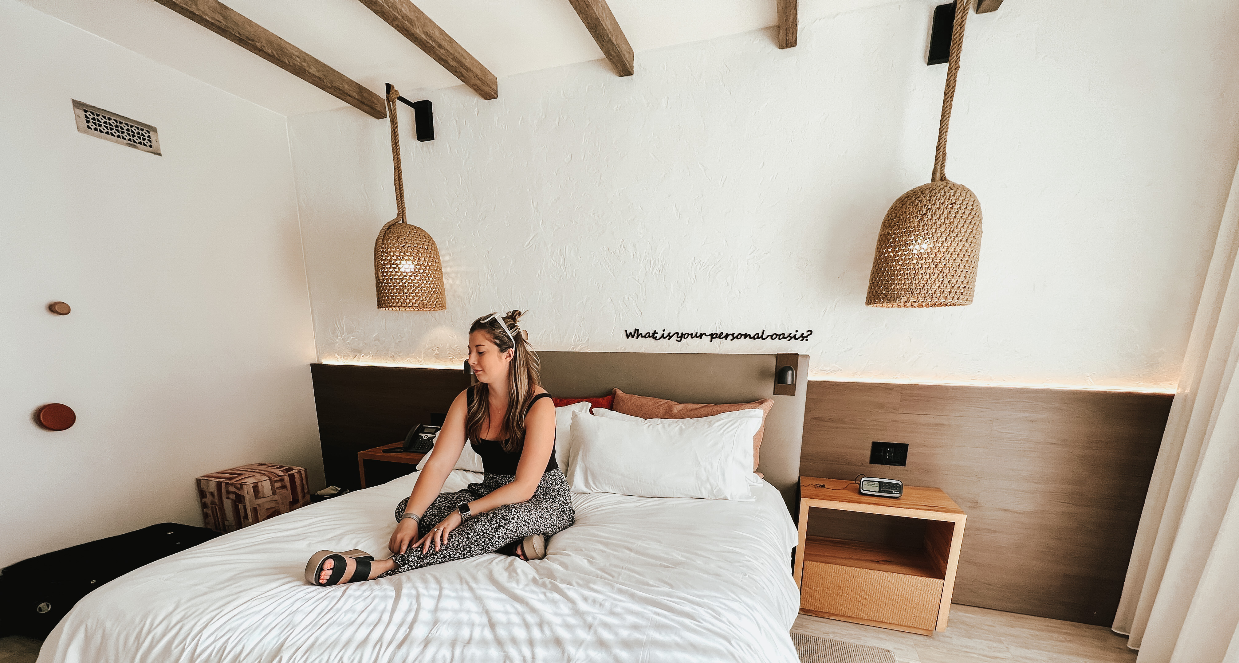 Advisor sitting on a bed in a modern hotel room with white and tan decor.