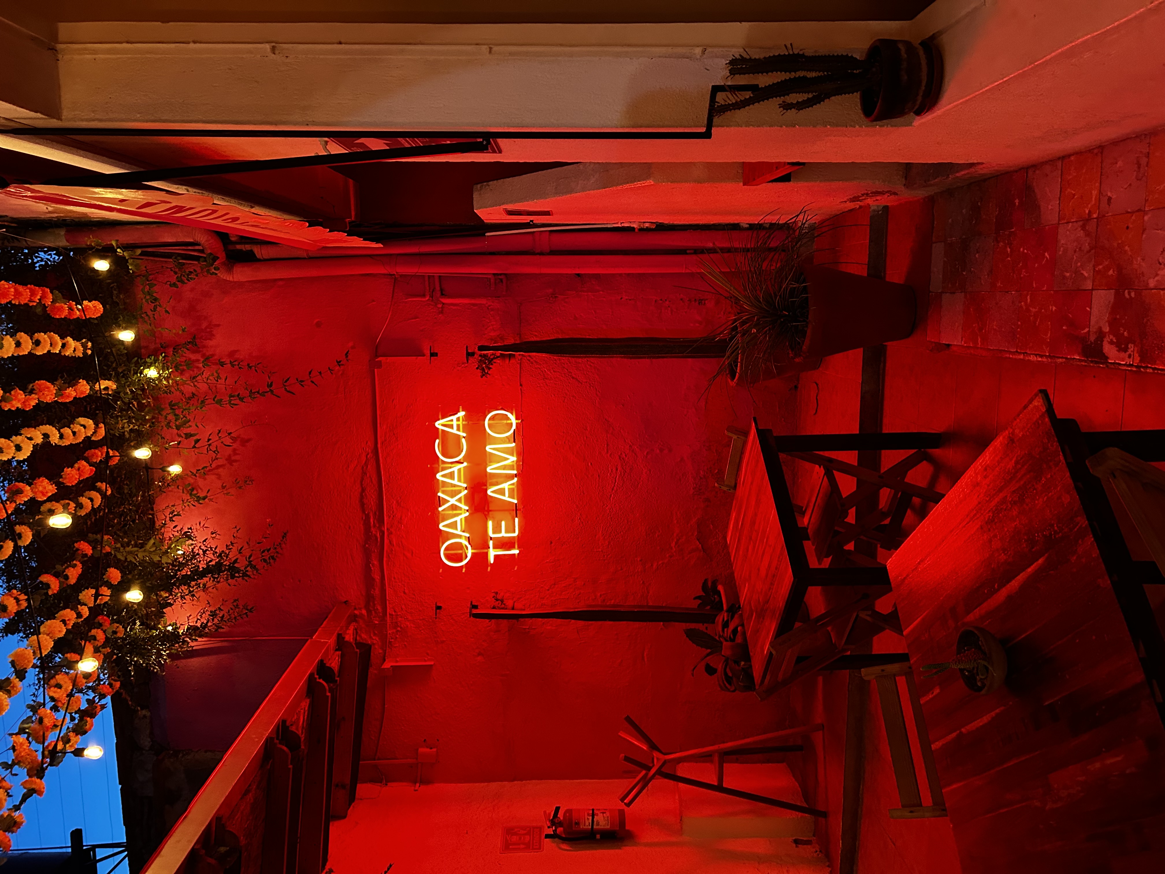 View of an indoor area with tables lit up red by a sign reading “OAXACA TE AMO”