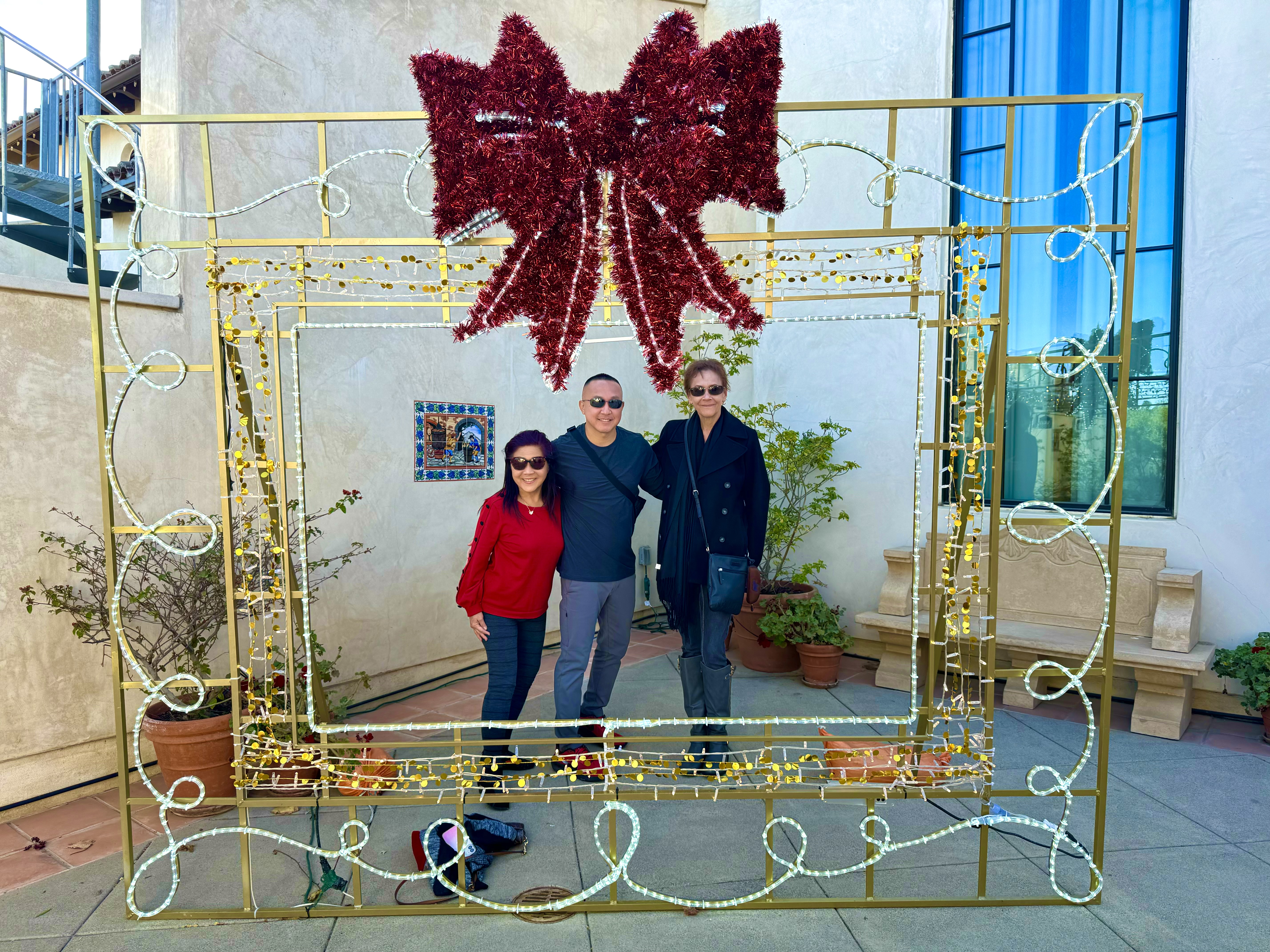 Scott and two others with their arms around each other posing behind a lit up frame in the shape of a present