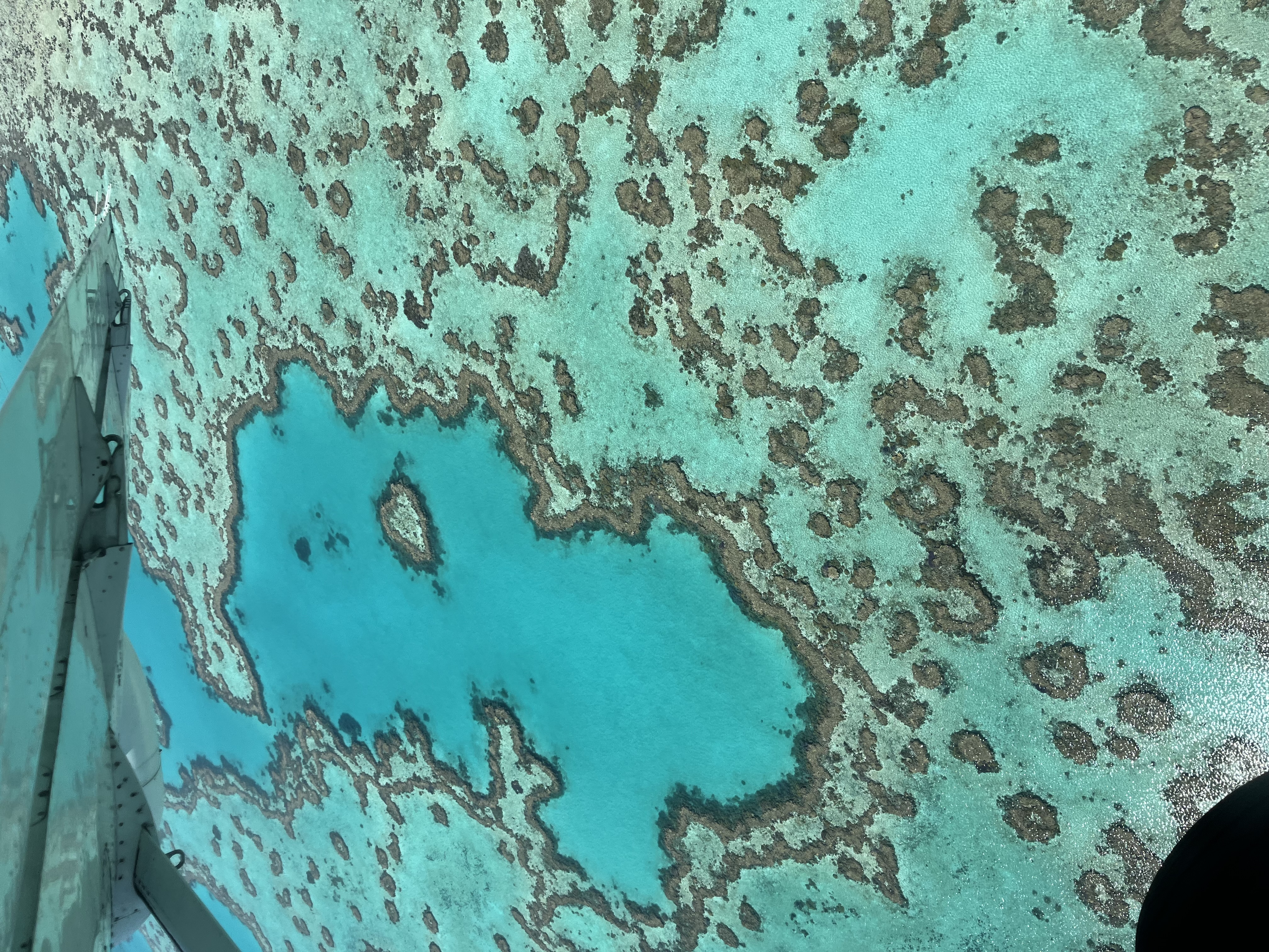 Gorgeous aerial view of a turquoise ocean with coral reef and rocks visible below the surface
