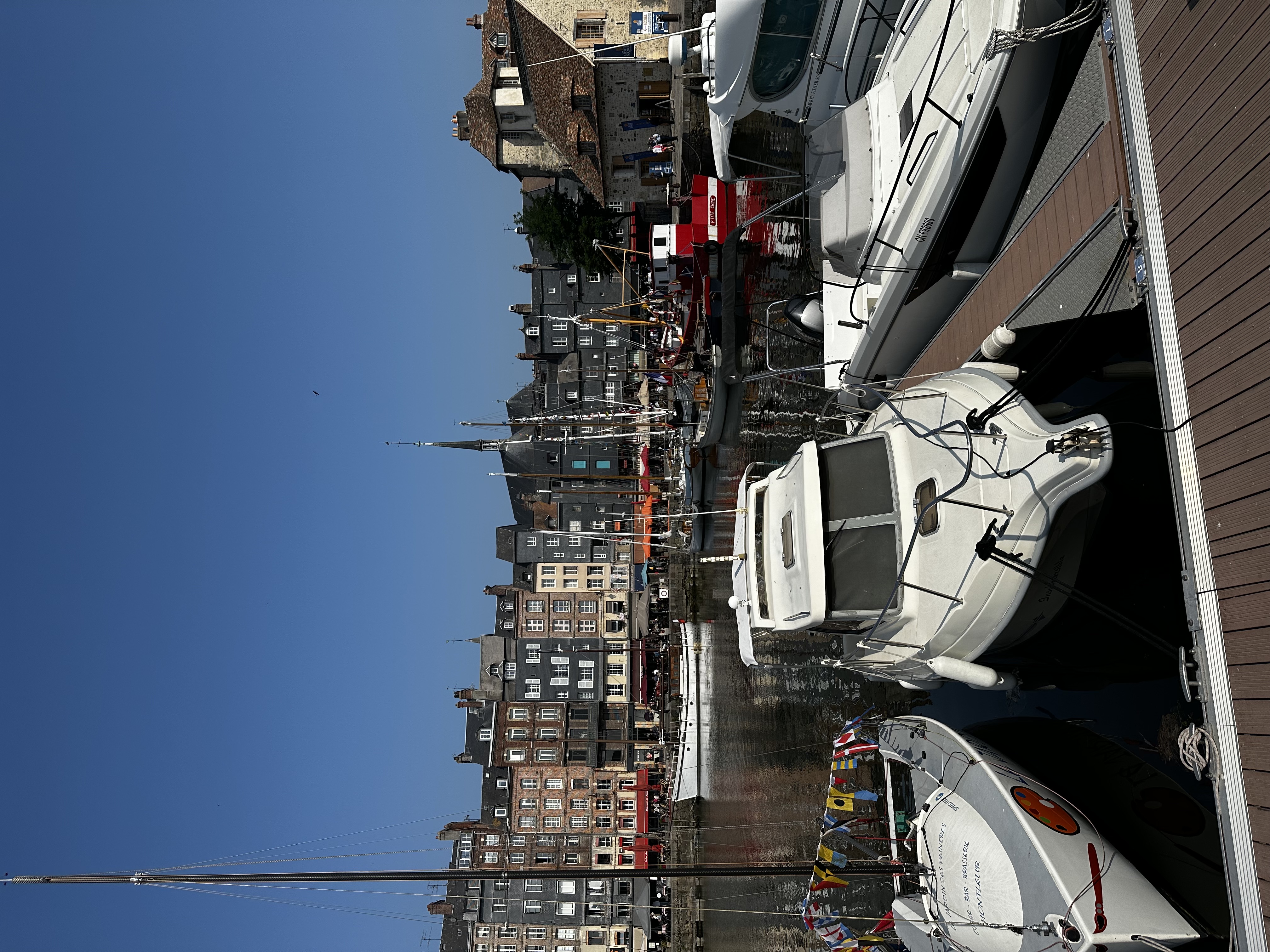 View of several large boats docked in a sunny harbor with narrow buildings lined up in the distance
