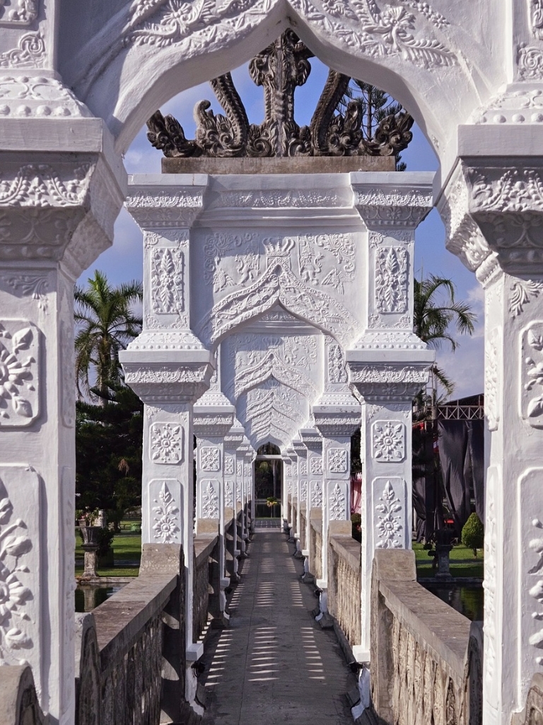 Beautiful view of a narrow pathway stretching through white carved columns on a sunny day