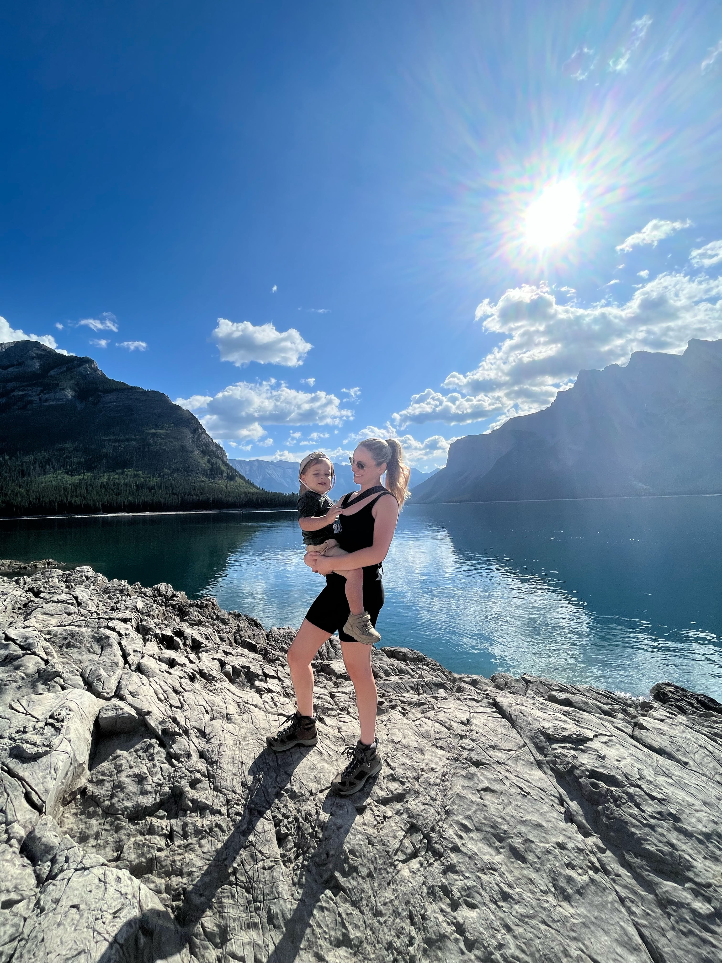 Woman and child by lake with mountains in the back during the day.