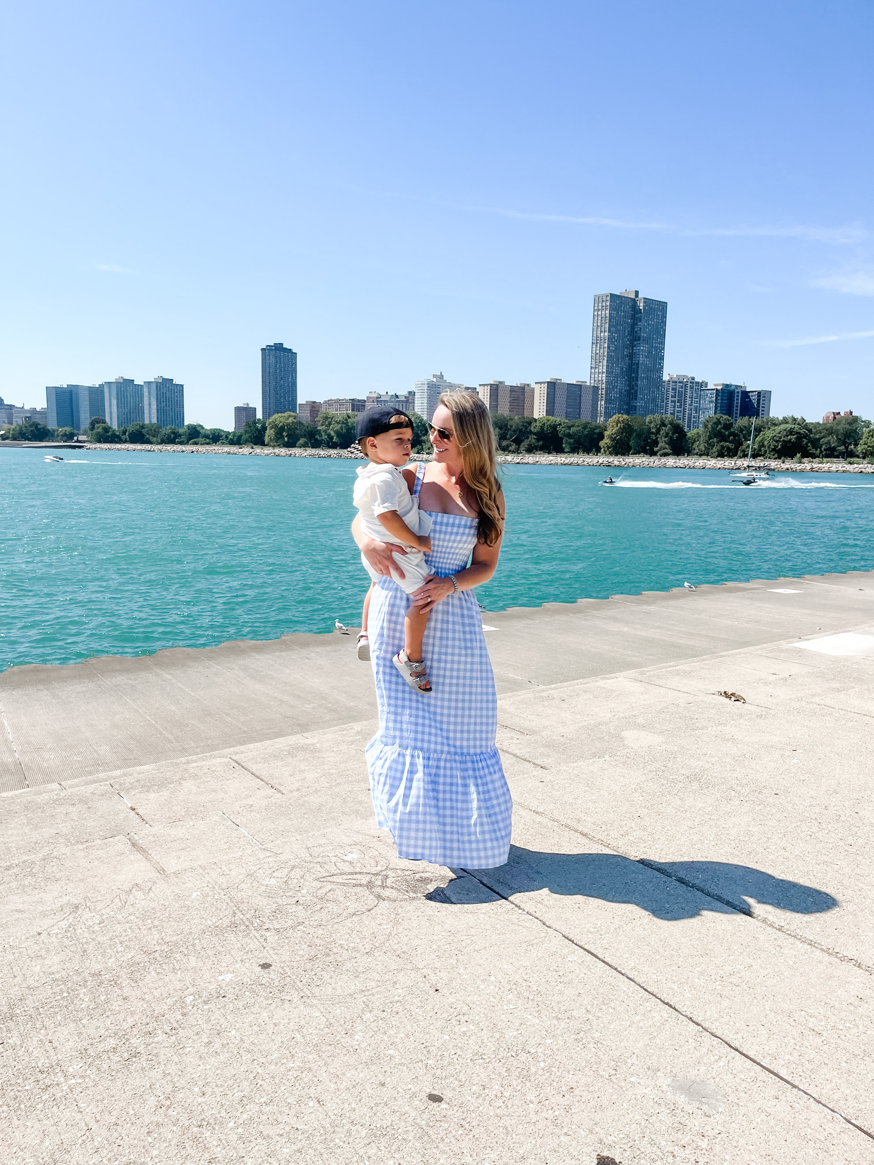 Woman with child with blue waters and tall buildings in the background.