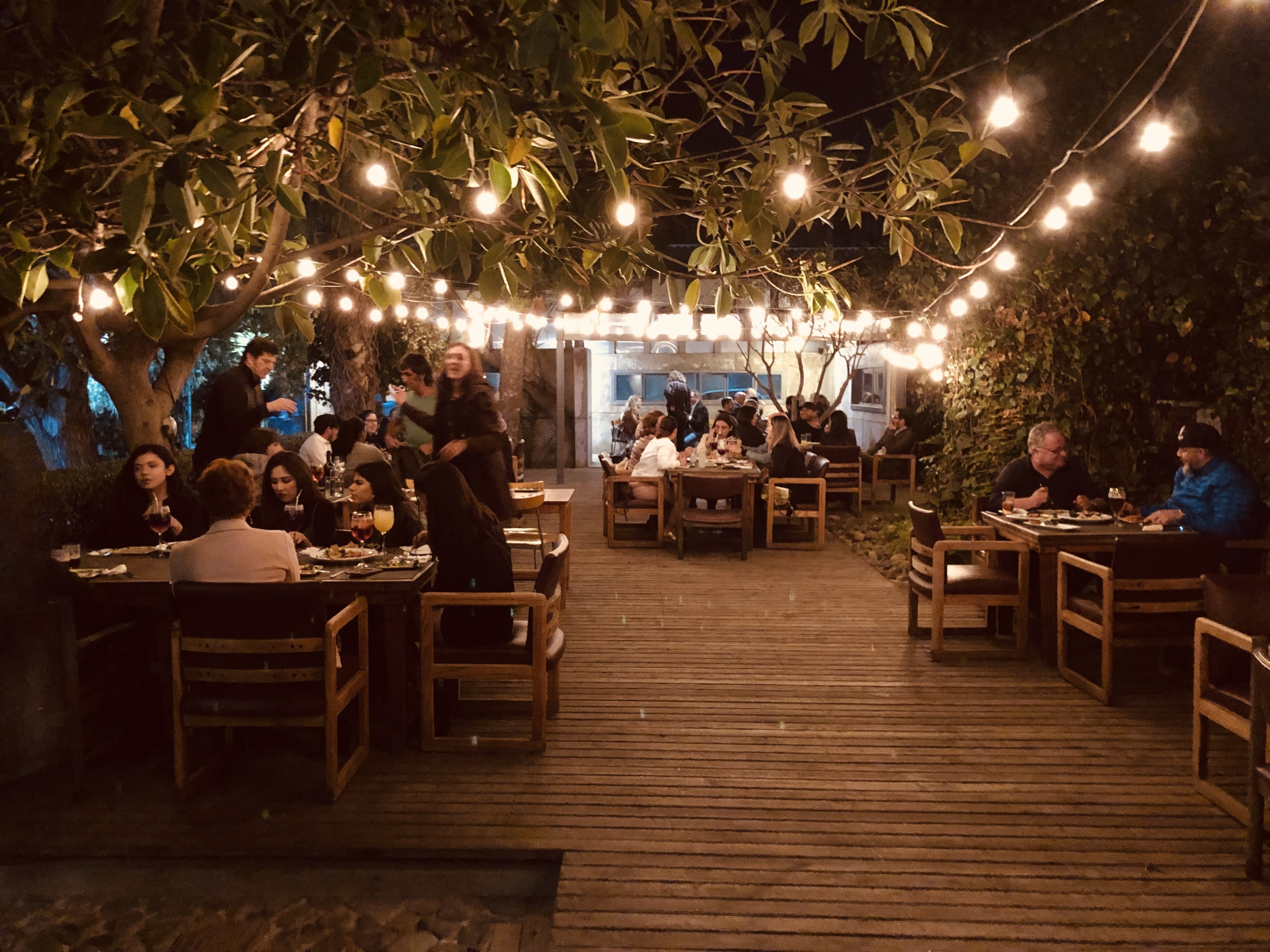 An outdoor restaurant with string lighting in the trees and wood deck.