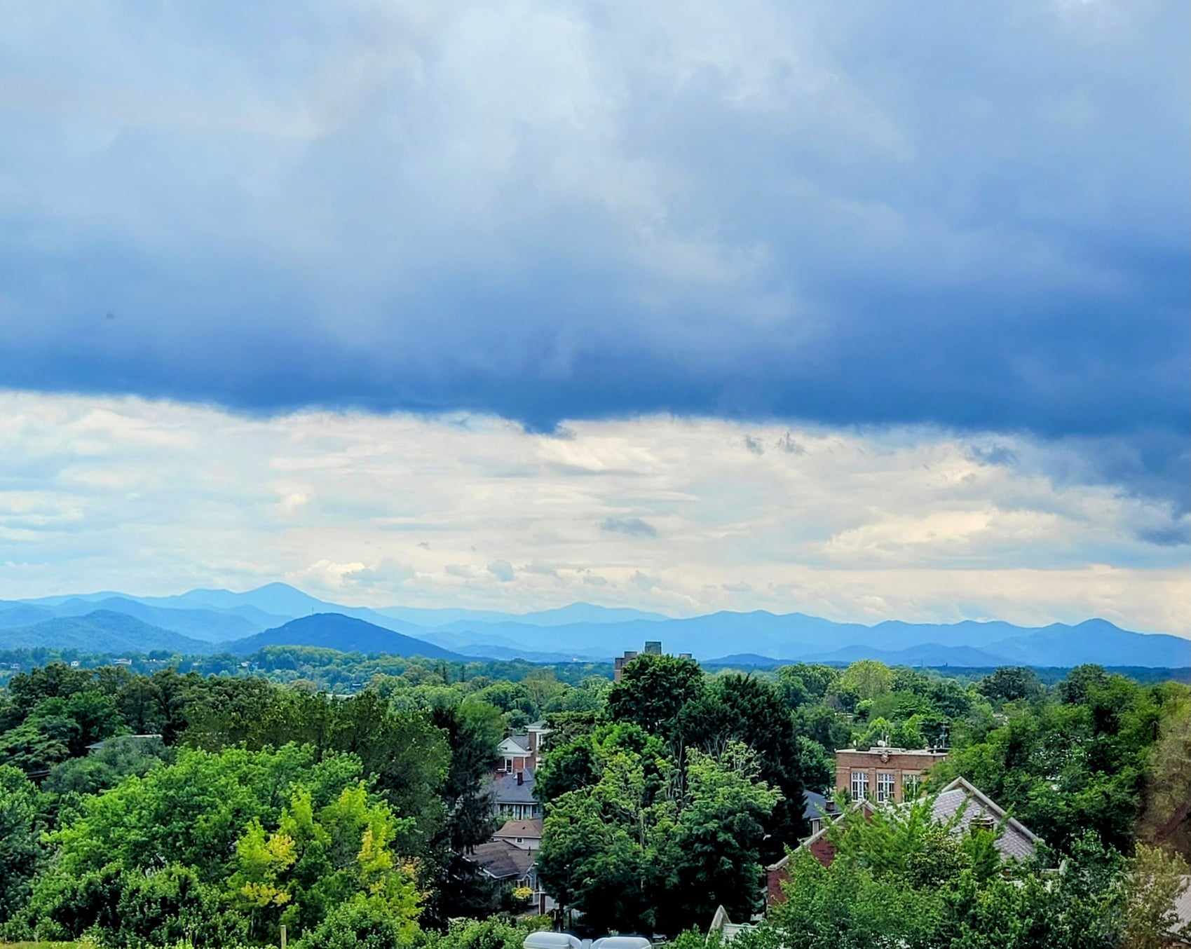 Forest and houses with rolling mountains in the background.