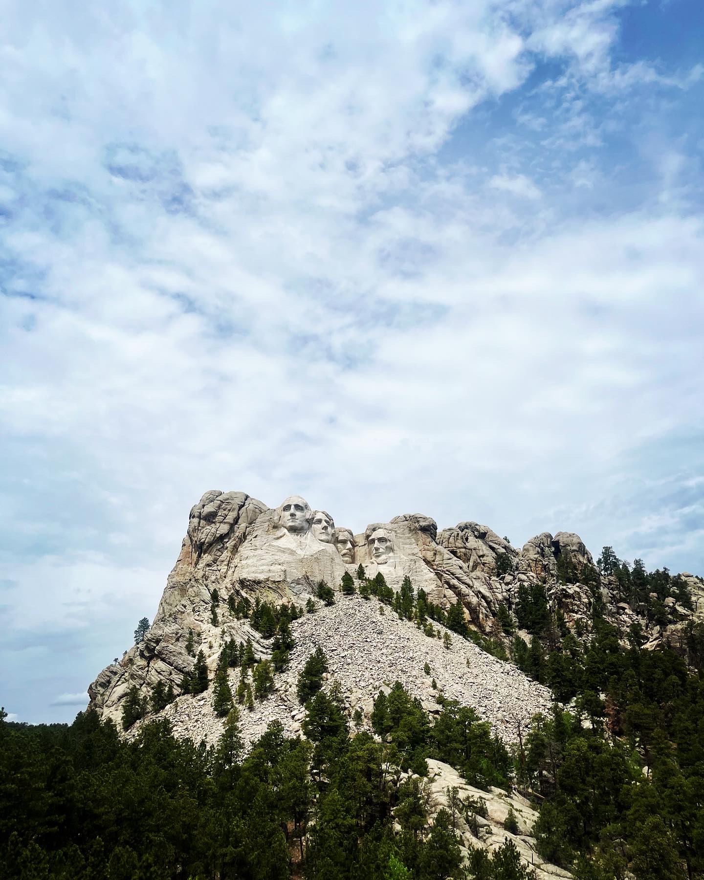 View of a rocky mountain with pine trees under sunny skies