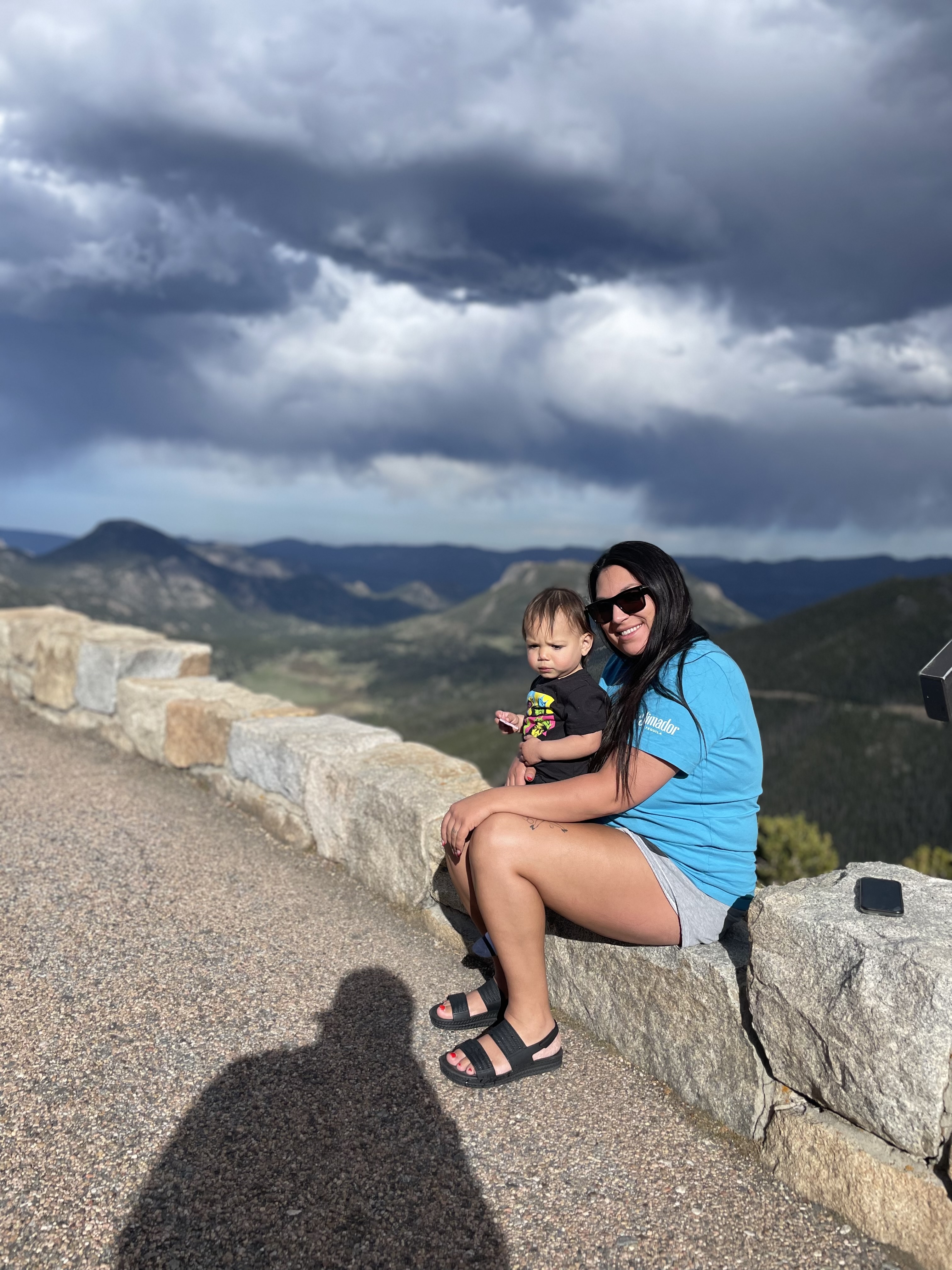 Olivia and her son sitting on a stone ledge overlooking a beautiful green valley with cloudy skies