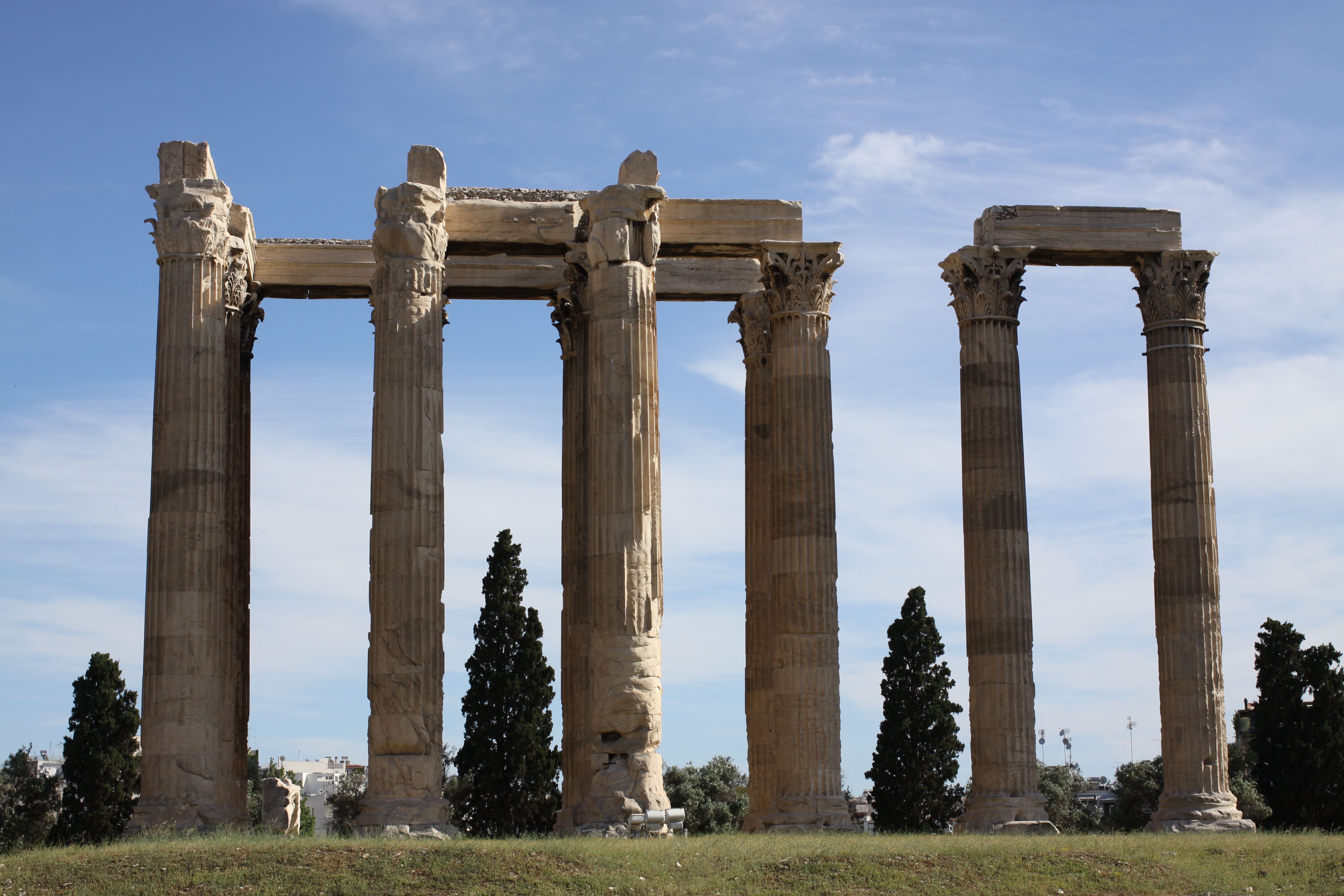View of large ancient columns at an archaeological site with nearby trees under sunny skies