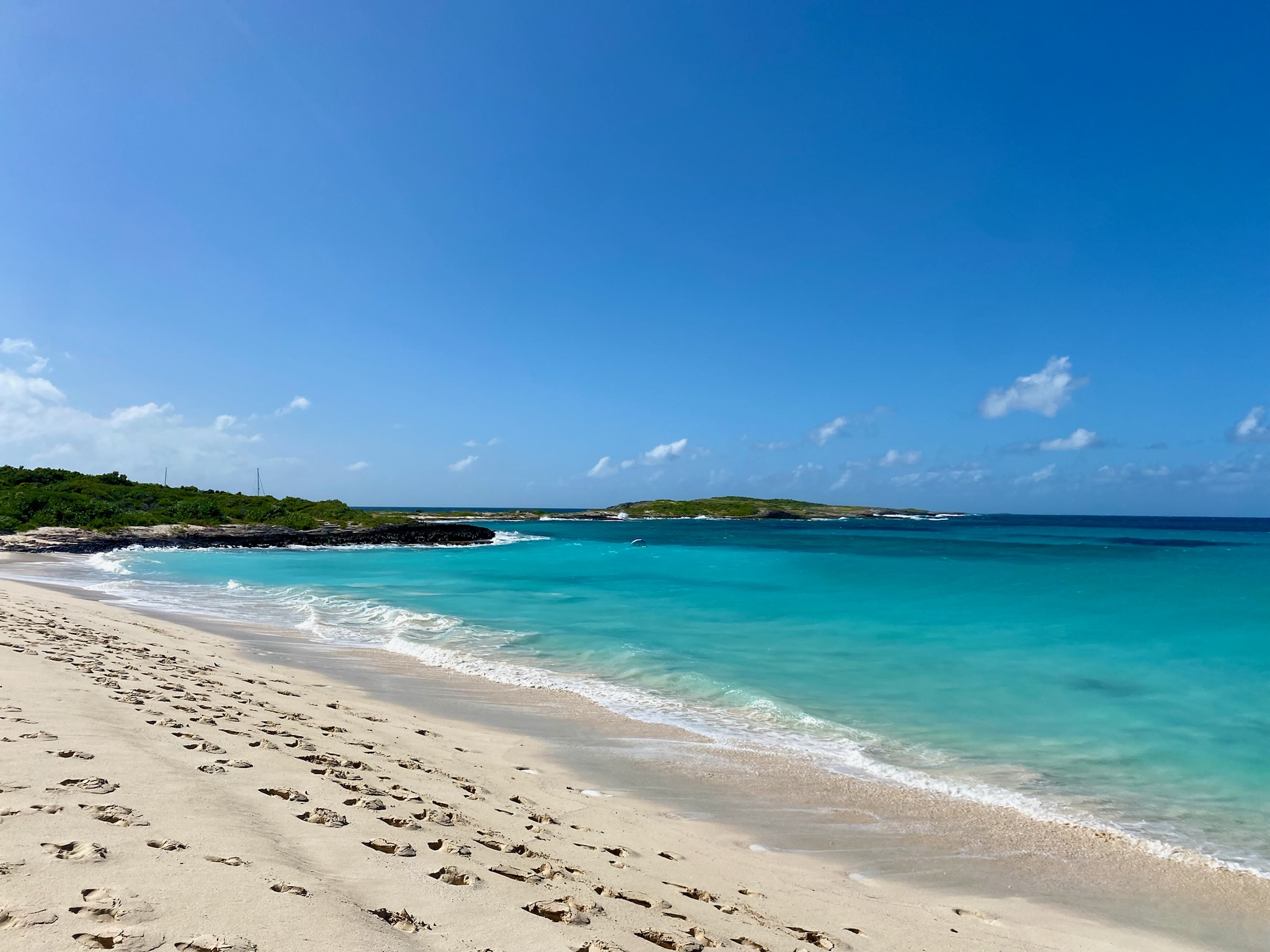 Beautiful view of a bright turquoise ocean besides a clean white sandy beach with footsteps in the sand on a sunny day