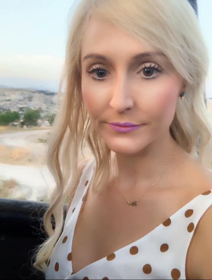Advisor with blonde hair posing in a white and brown polka-dotted top.