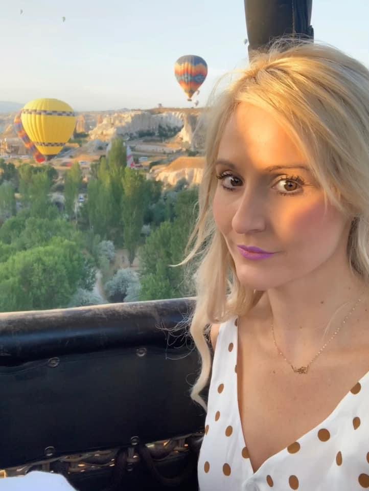 Advisor with blonde hair and polka-dotted top posing in front of several hot air balloons in the background.