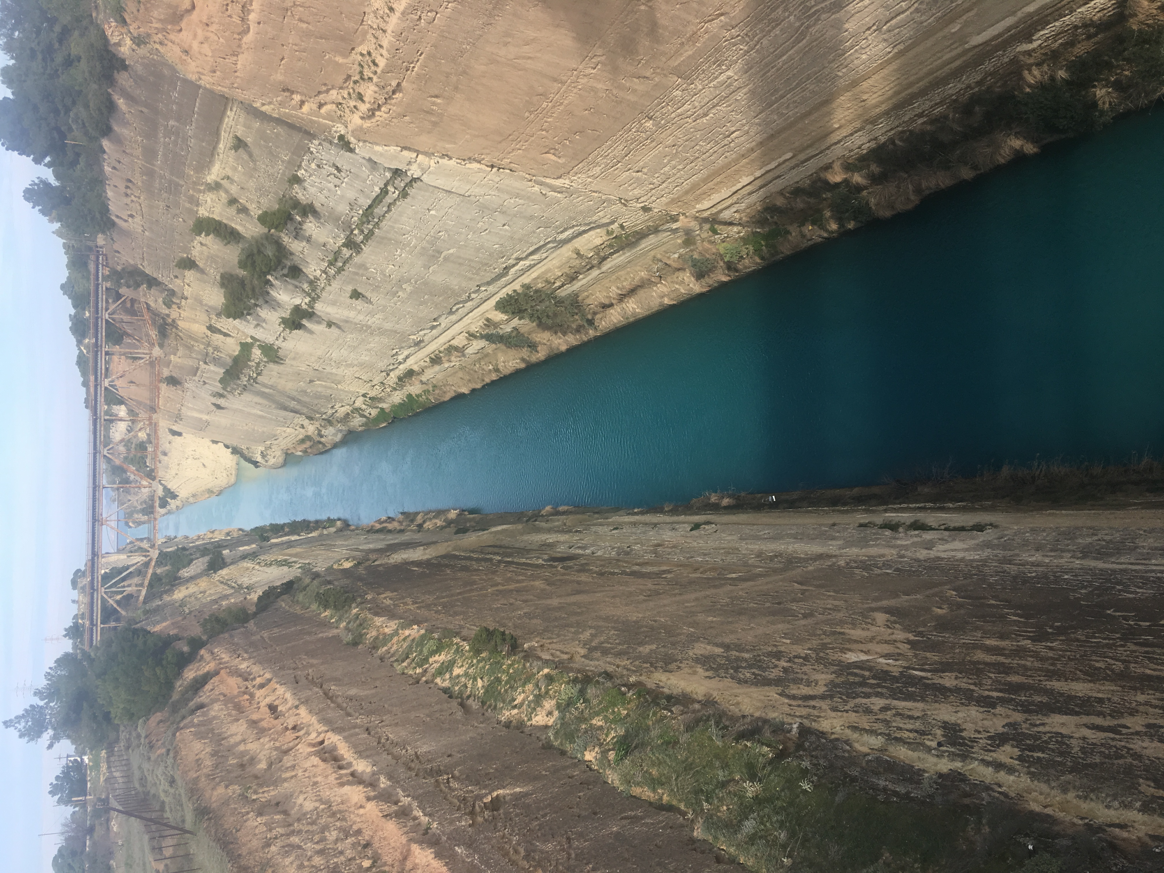 Narrow turquoise canal running between steep rock walls under a cloudy sky.
