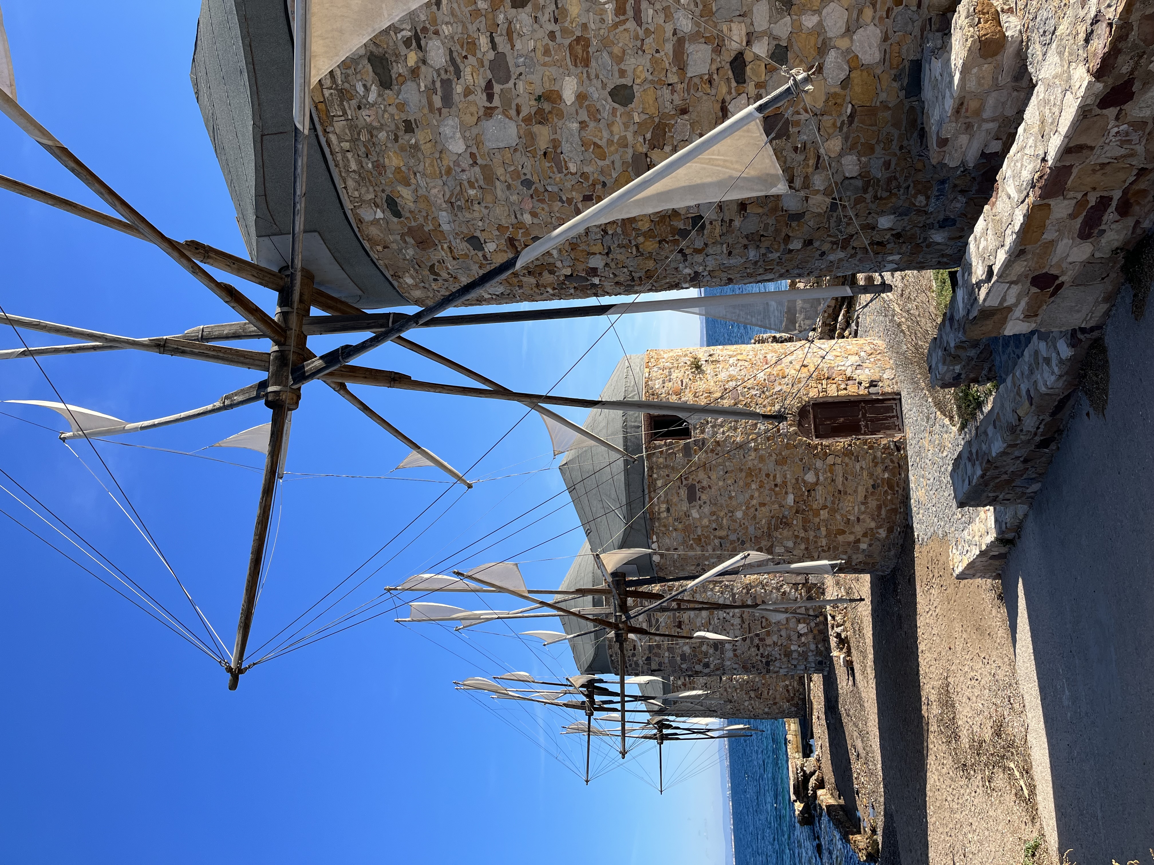 Historic stone windmills with wooden sails by the seaside on a clear, sunny day.