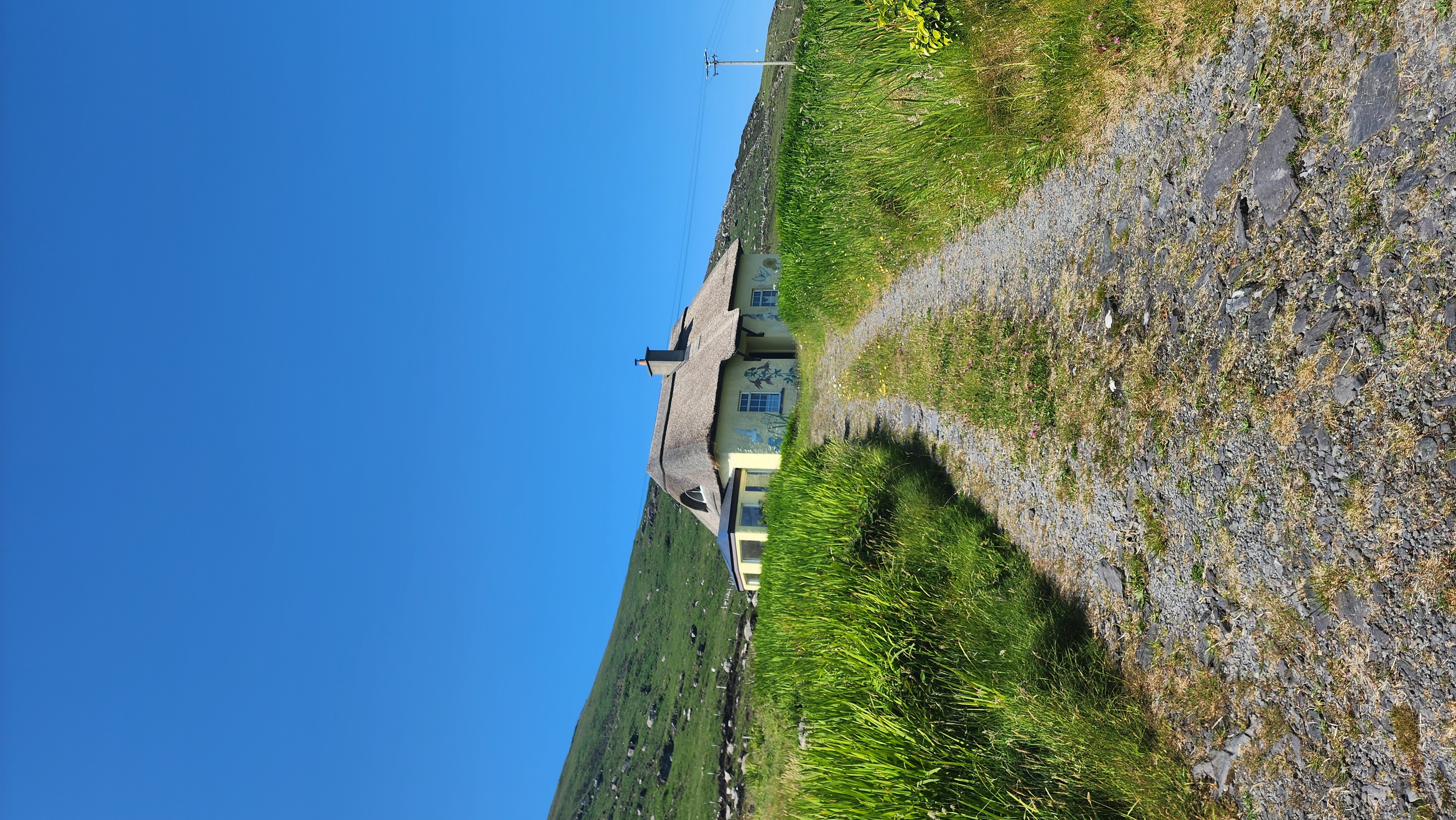 Narrow gravel pathway in between grassy fields leading to a small white building under clear skies